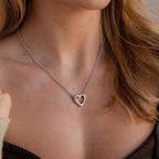 A woman wears the Rolo Heart Clasp Necklace, featuring a heart-shaped clasp, with a brown off-shoulder top.