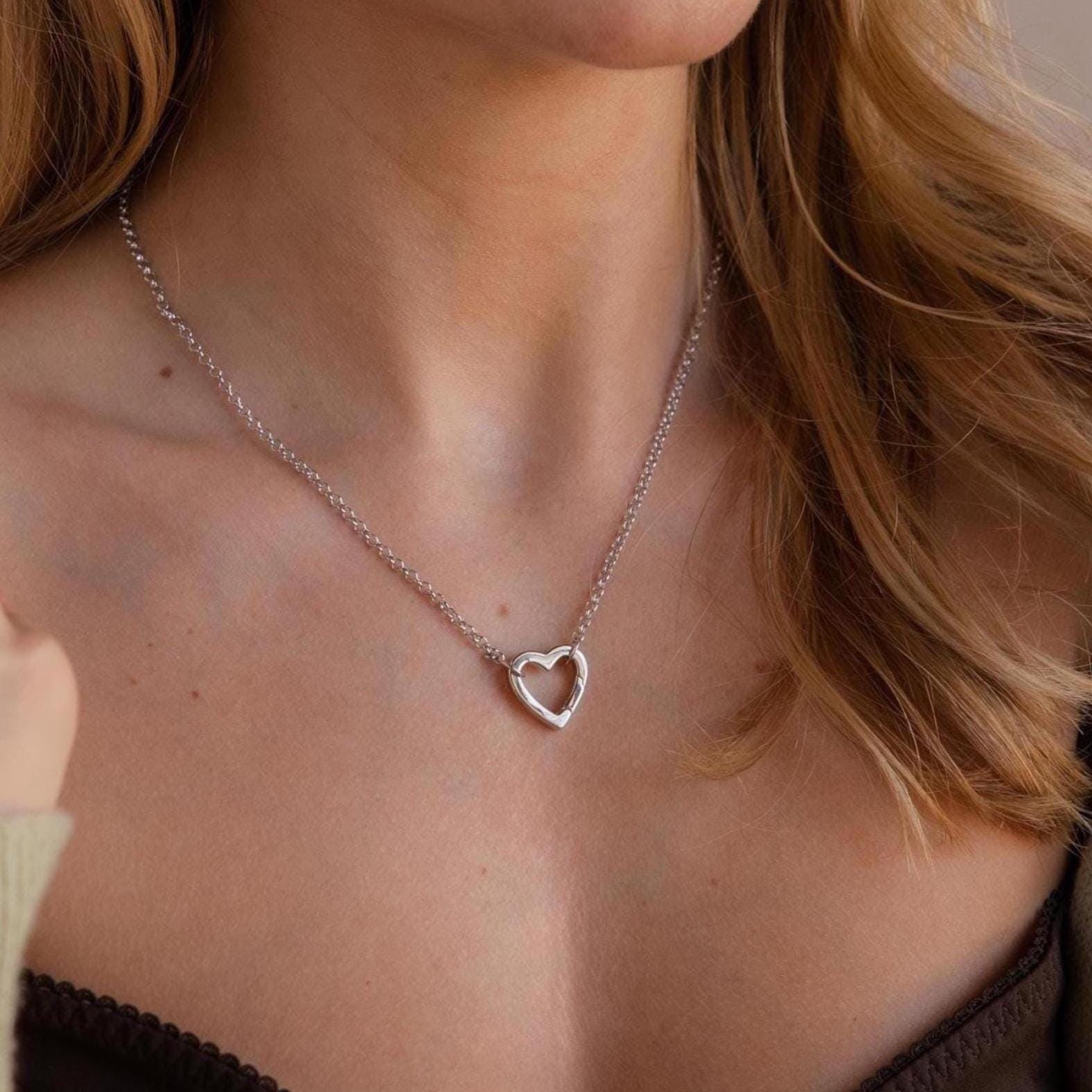 A woman wears the Rolo Heart Clasp Necklace, featuring a heart-shaped clasp, with a brown off-shoulder top.