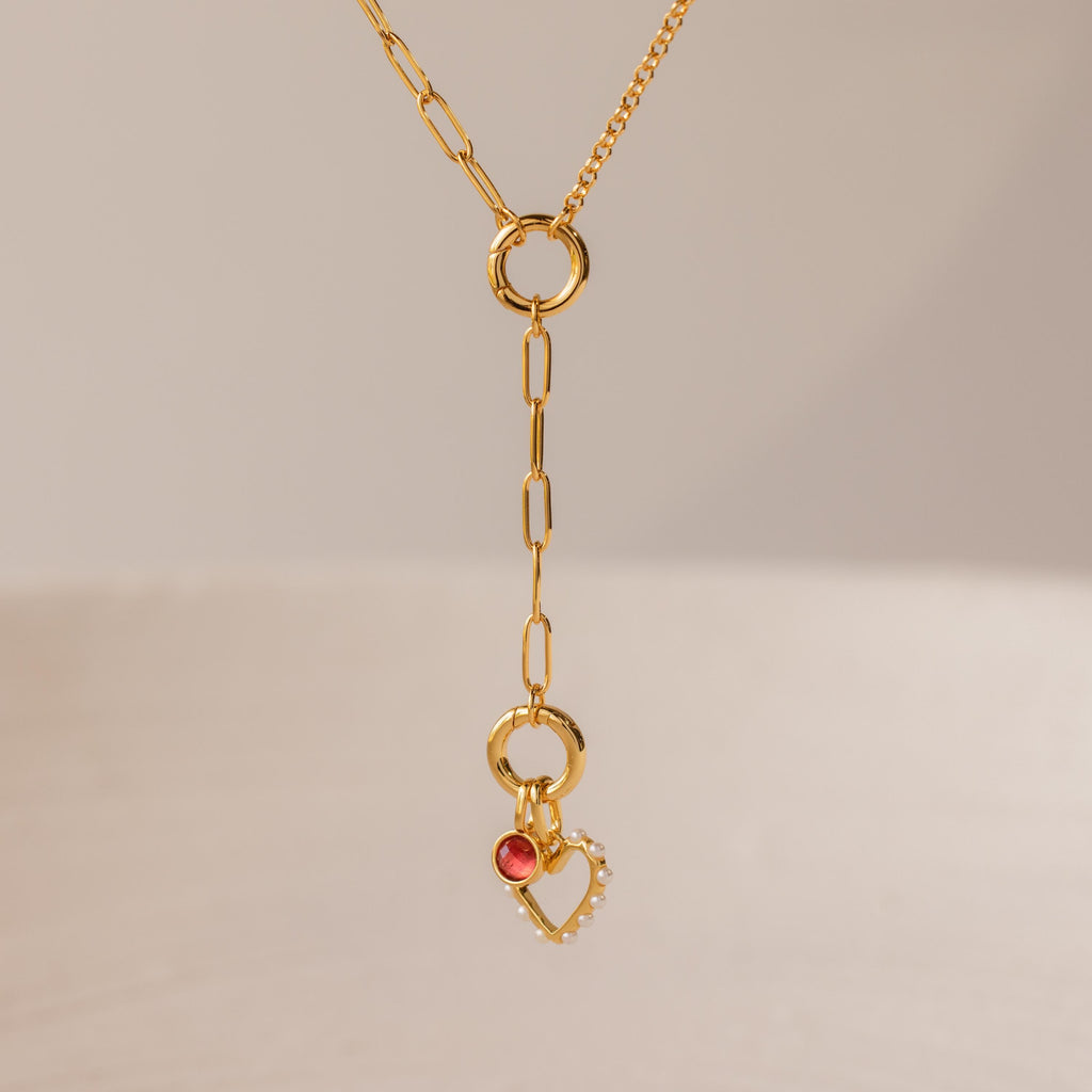 Rolo Lariat Paperclip Clasp Necklace featuring a gold chain with a dangling heart charm, pearls, and a small red gemstone, displayed on a neutral background.