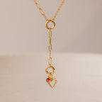 Rolo Lariat Paperclip Clasp Necklace featuring a gold chain with a dangling heart charm, pearls, and a small red gemstone, displayed on a neutral background.