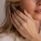 A woman with light skin touches her face, displaying the Dainty Marquise Topaz Ring featuring small green stones—an elegant birthstone piece perfect for everyday Art Deco style.