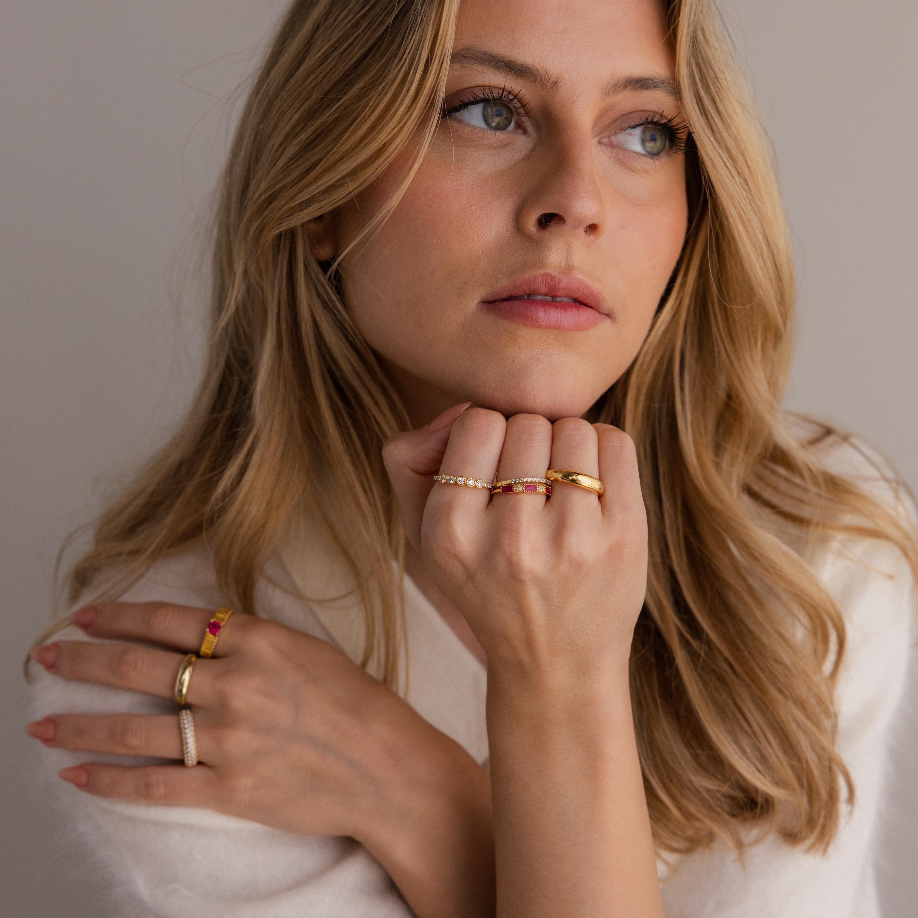 A blonde woman in a white top wears the Mixed Art Deco Birthstone Ring in Rose Gold, gazing thoughtfully to the side.