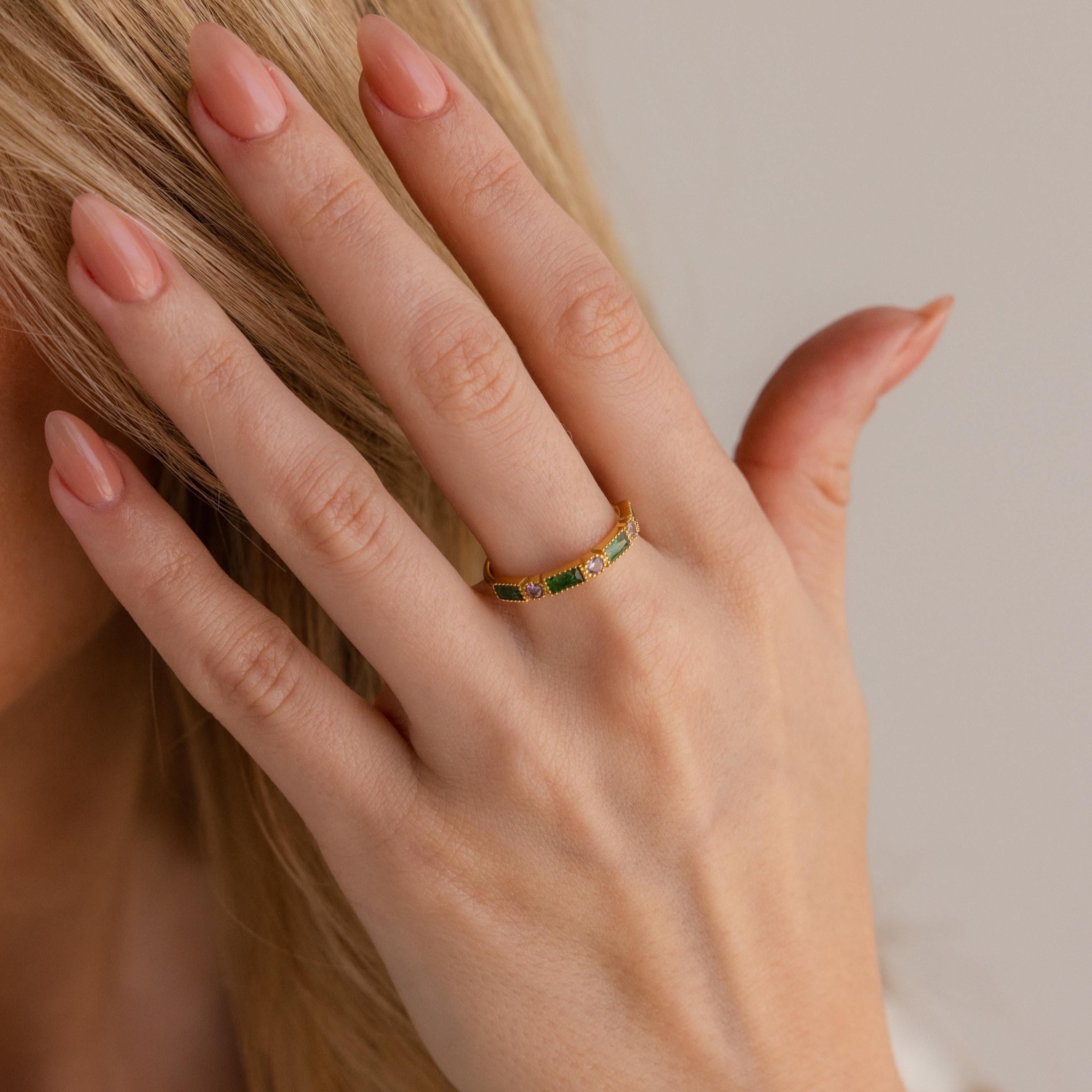 A manicured hand wears the Mixed Art Deco Birthstone Ring with green stones, shown near blonde hair.