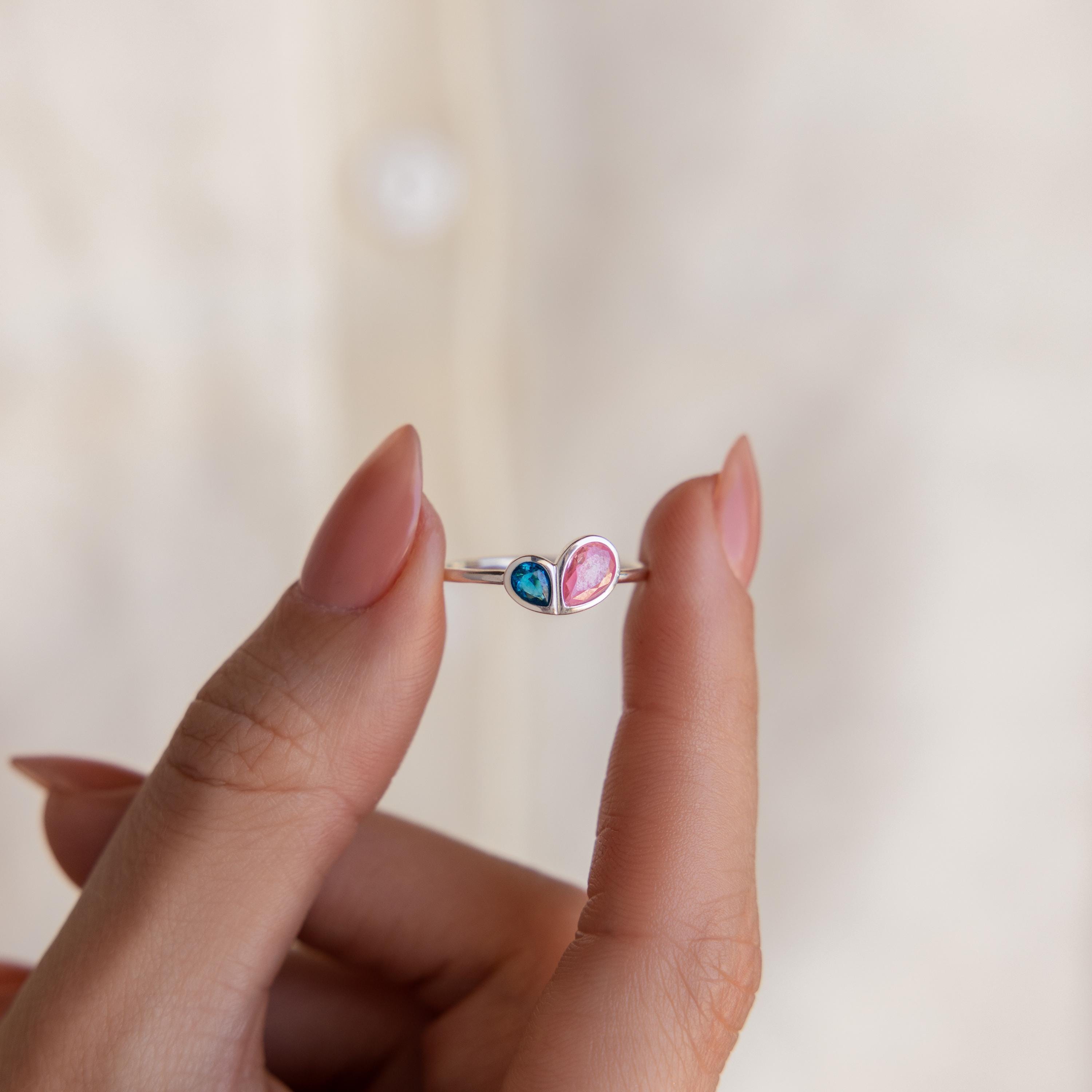 A hand holds the Toi et Moi Heart Birthstone Ring in Sterling Silver, featuring two heart-shaped stones—one blue and one pink.