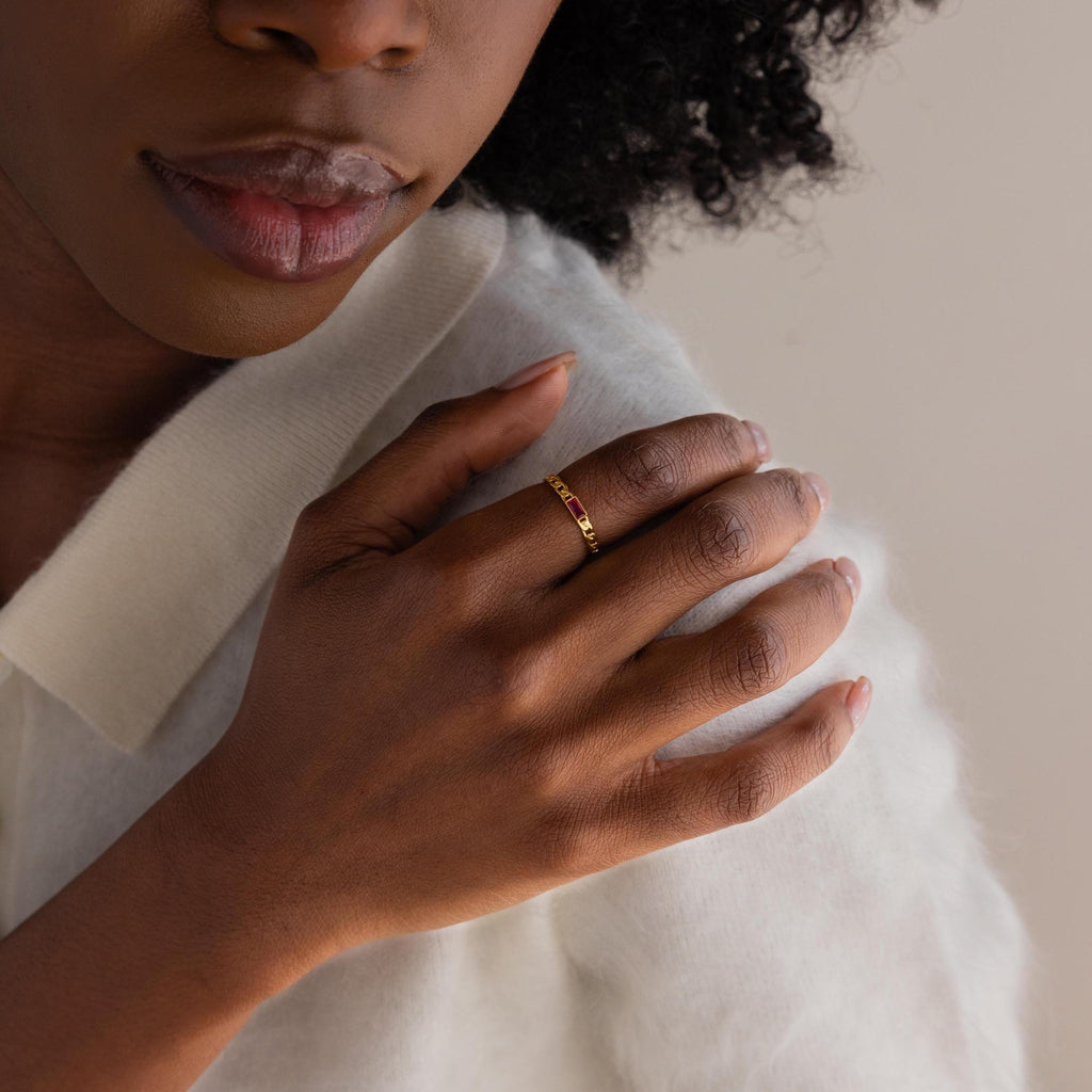 A woman wearing a Baguette Birthstone Curb Ring gently rests her hand on her shoulder, dressed in a white sweater.