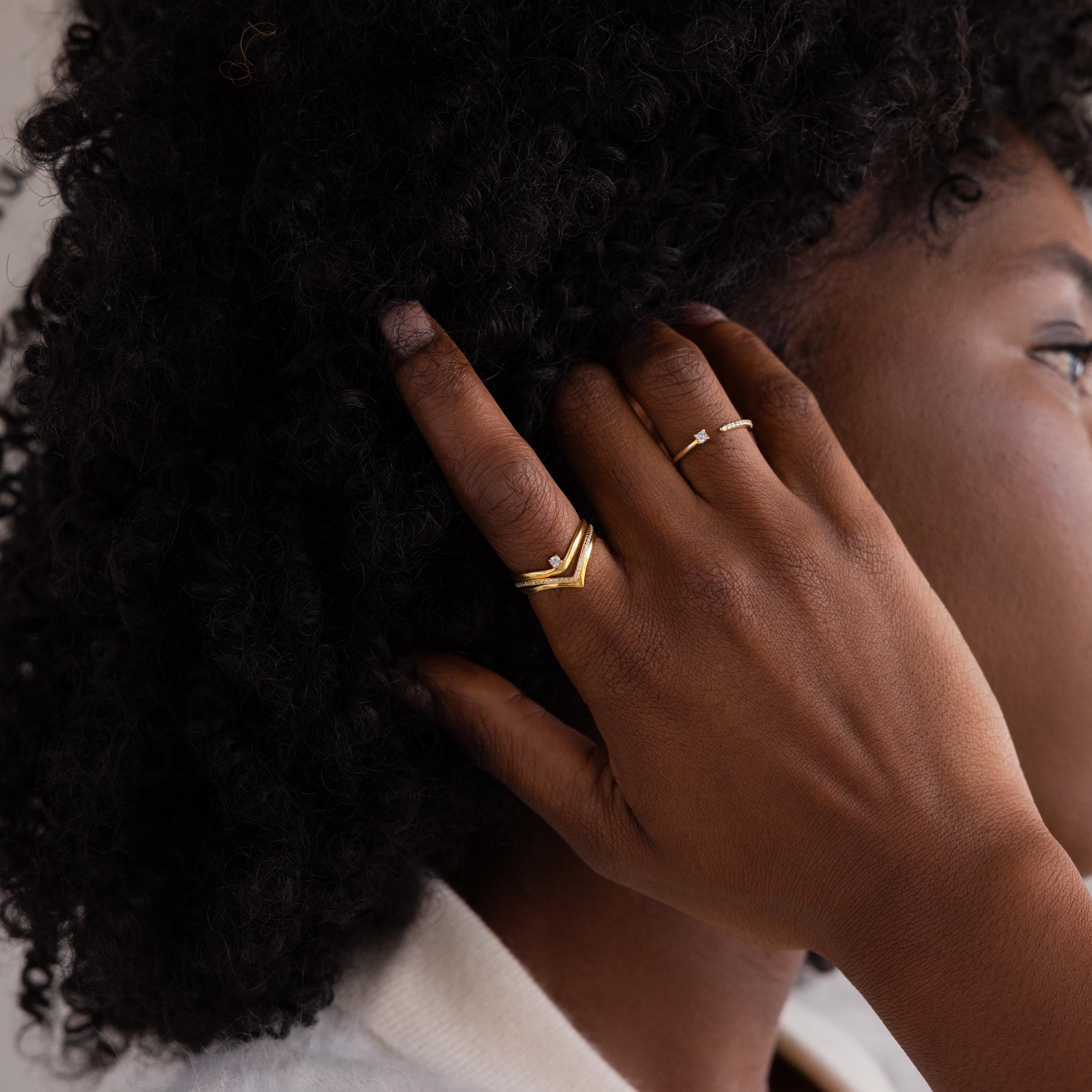A hand adorned with the Onyx Drop Curve Ring touches curly hair near the ear; the person wears a white top.