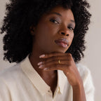Woman with curly hair in a cream shirt rests her chin on her hand, highlighting the elegant Onyx Drop Curve Ring.