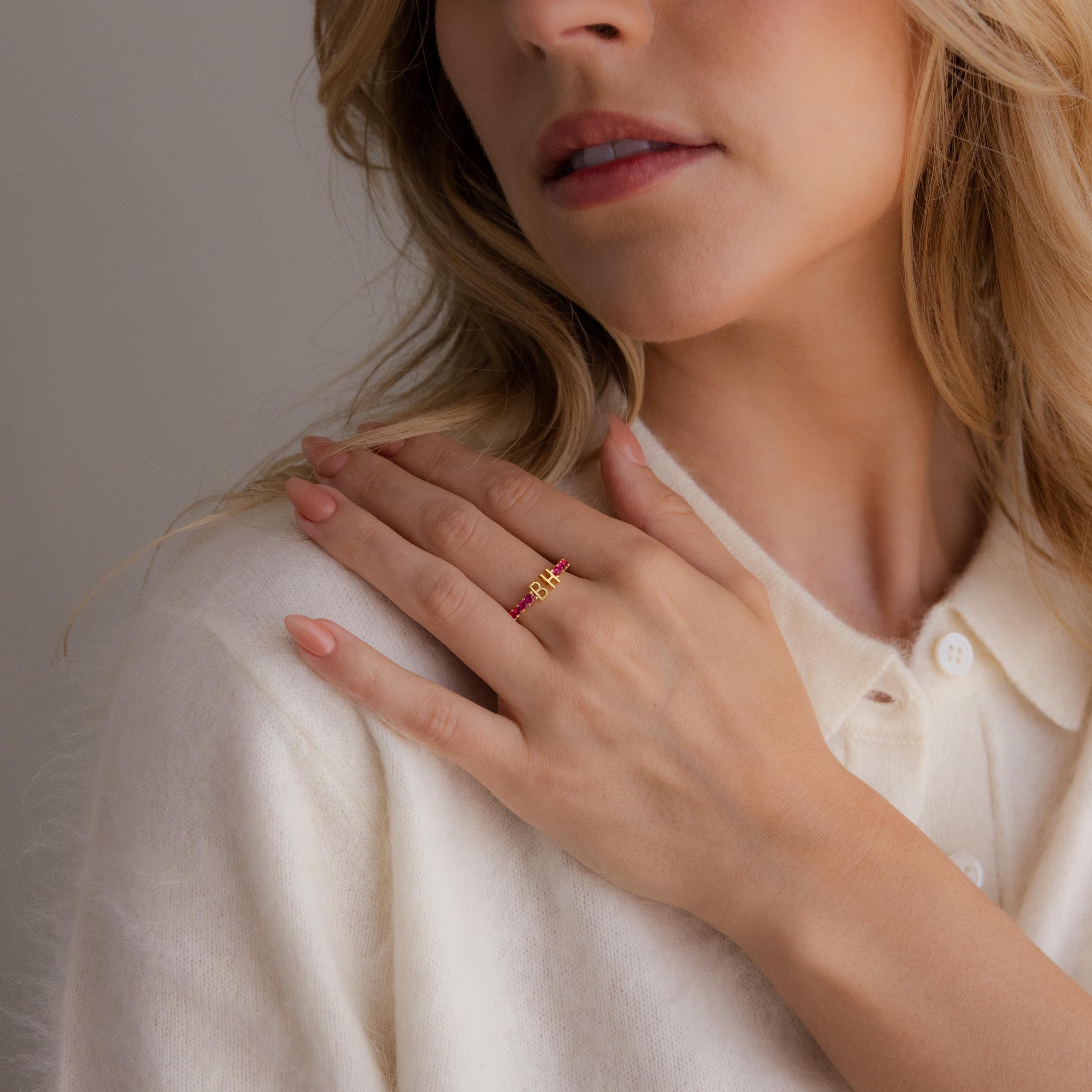 A woman in a cream sweater touches her collar, showcasing the Duo Initial Topaz Tennis Ring on her finger.