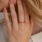 A hand with manicured nails wears the Duo Initial Onyx Tennis Ring, a personalized eternity band featuring pink beads and gold letters B and H.