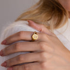 A woman showcases the elegance of the Pave Initial Signet Ring in 18K Gold, featuring a decorative engraving on her index finger.