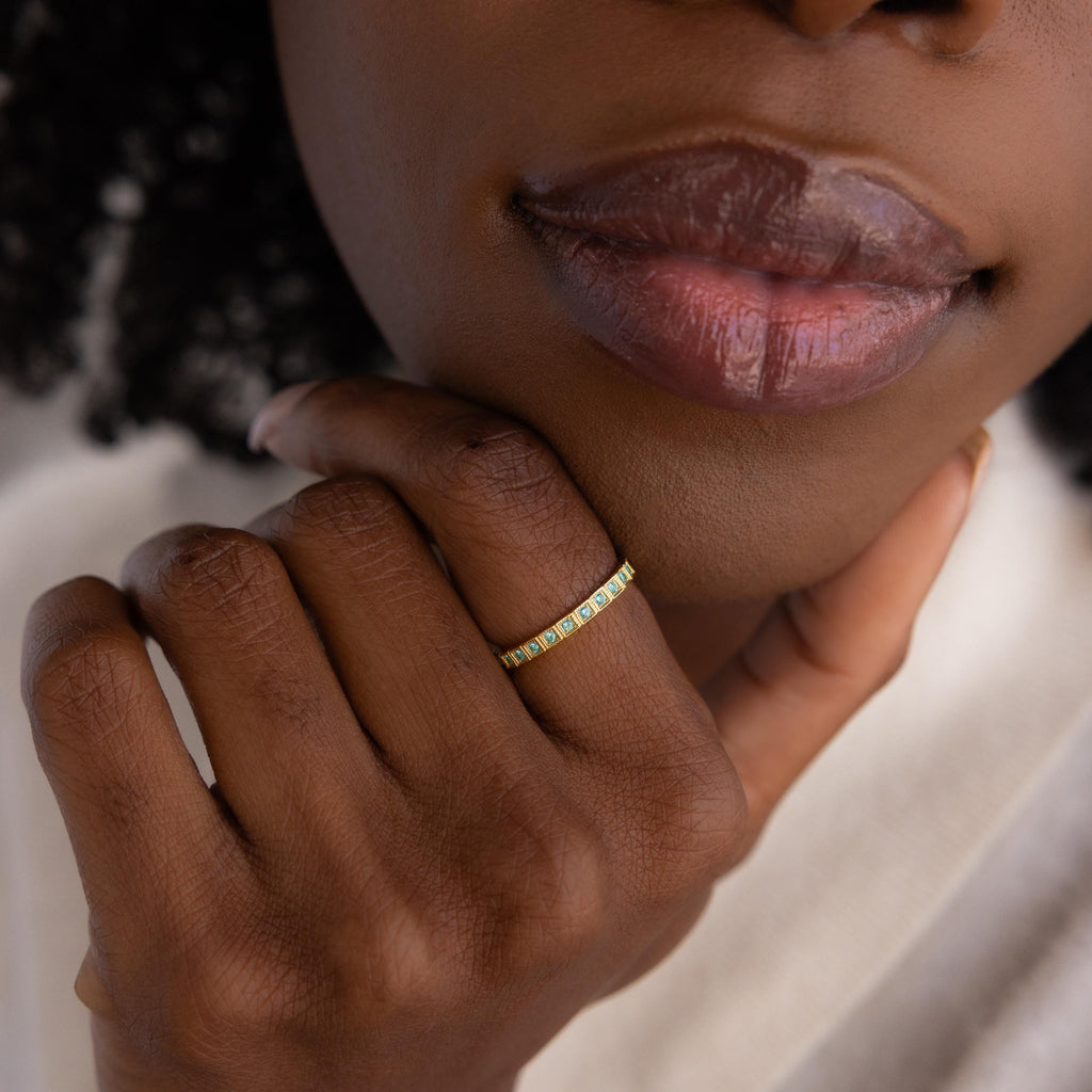 A close-up of a hand wearing the Art Deco Diamond Eternity Ring, its vintage-inspired gold band gently touching the chin of a person with full lips.