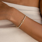 Close-up of a Diamond Tennis Initial Bracelet with shimmering diamonds and an infinity symbol, worn on a wrist with light fabric.