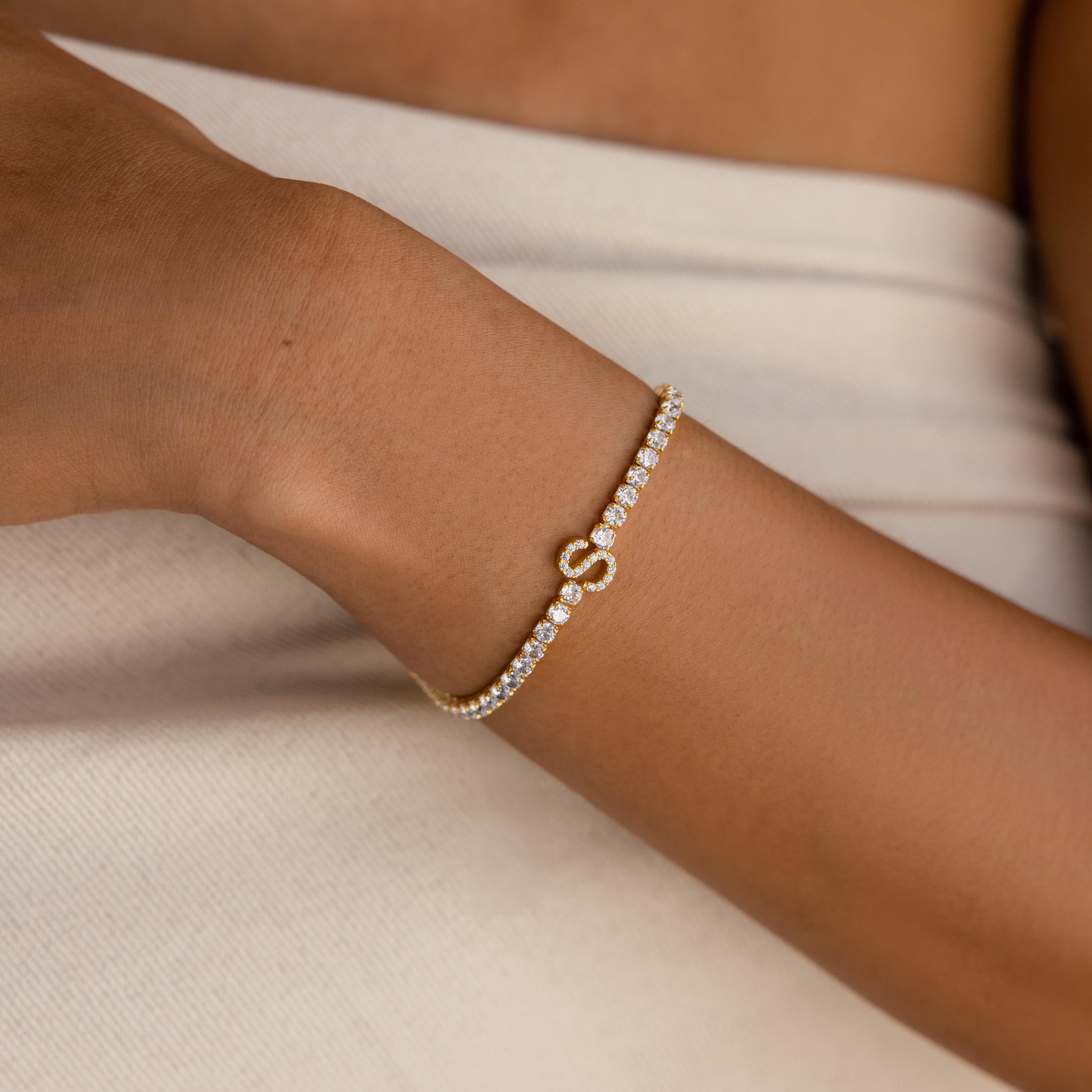 Close-up of a Diamond Tennis Initial Bracelet with shimmering diamonds and an infinity symbol, worn on a wrist with light fabric.
