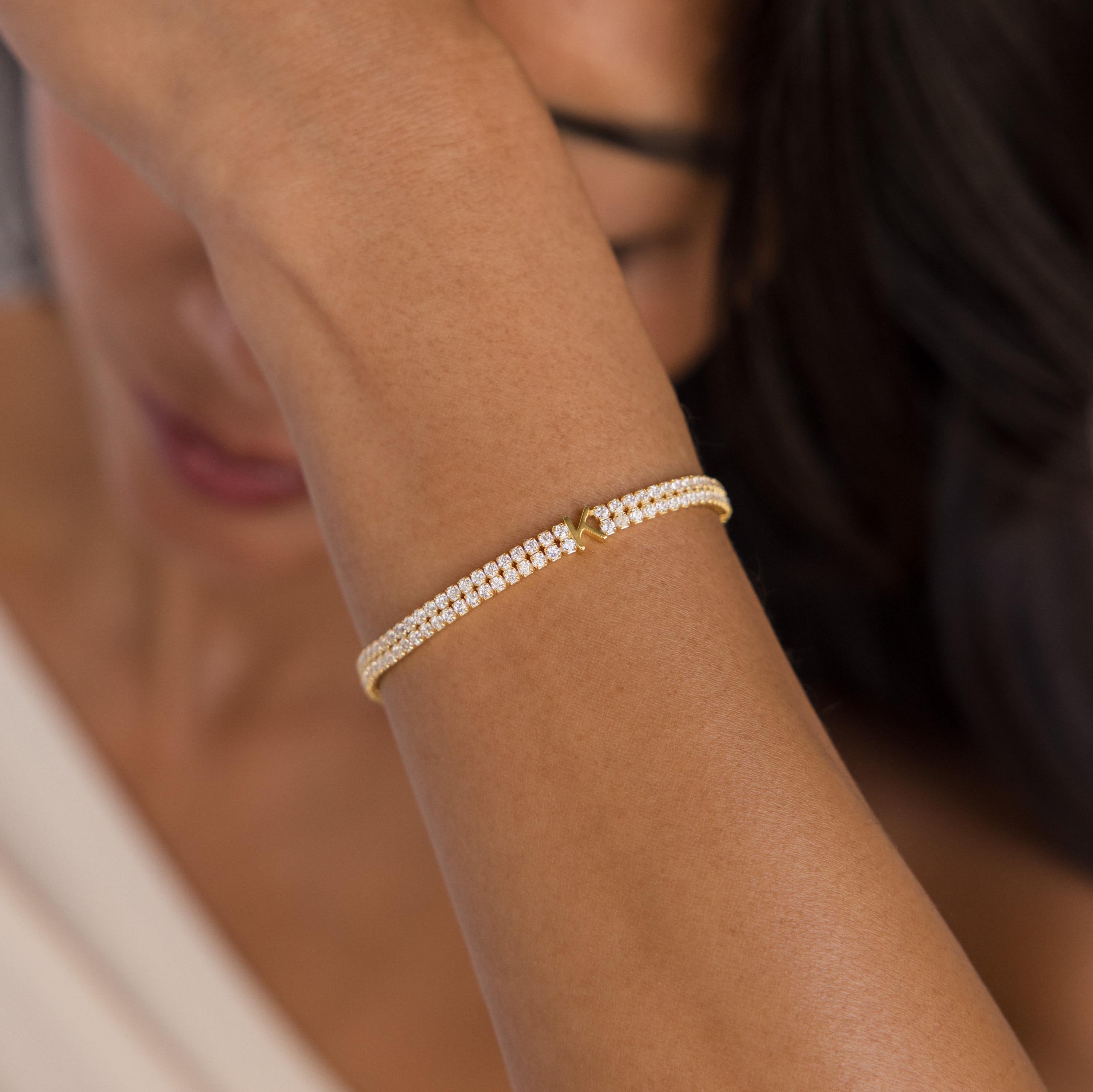 A woman wears the Initial Duo Tennis Bracelet, featuring a double-chain design with gold and diamonds, as she covers part of her face with her arm.