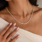 A woman wearing a Diamond Tennis Letter Necklace touches her chest with manicured nails.