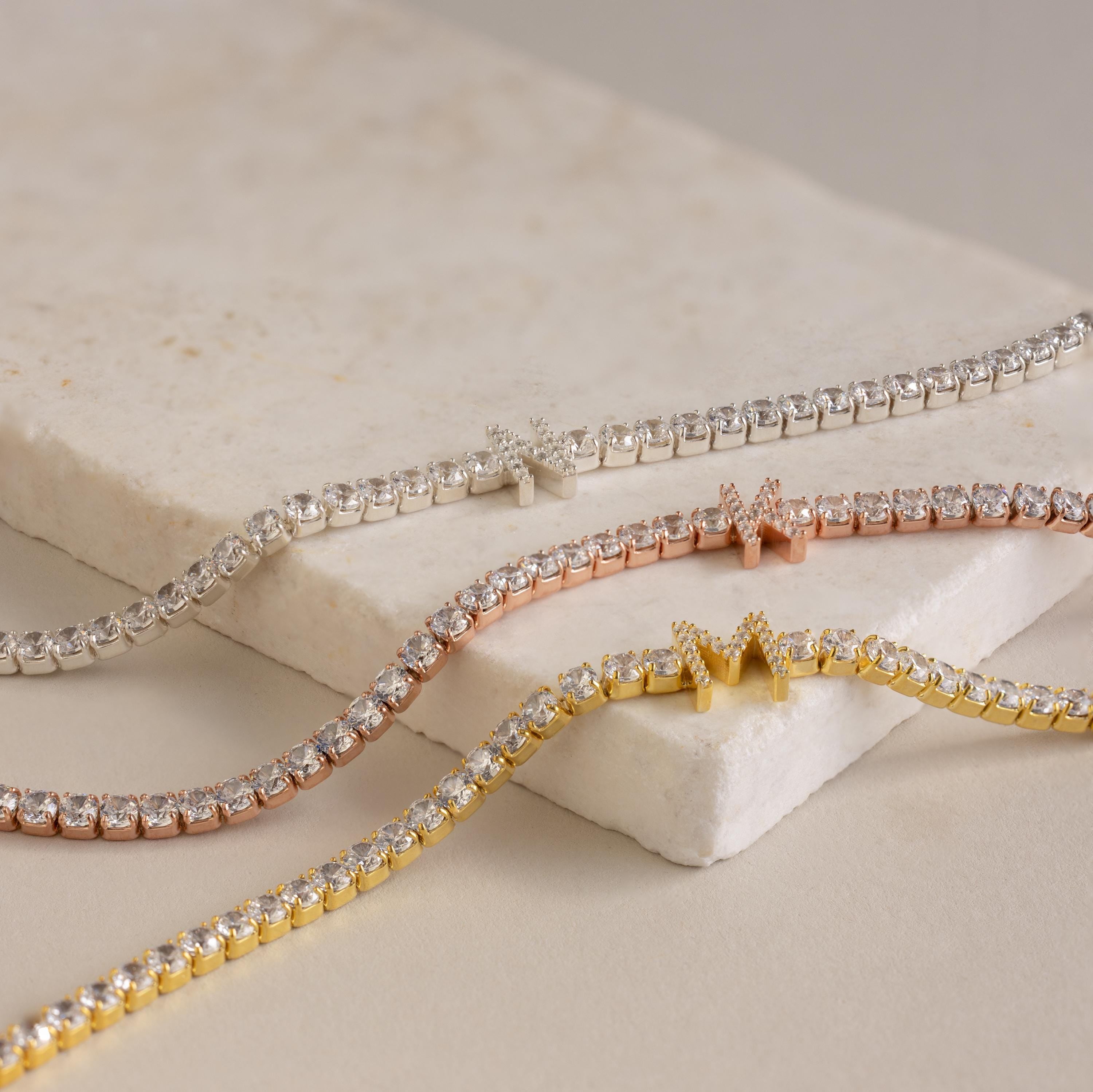 The Diamond Tennis Initial Necklace shines alone or stacked with silver, rose gold, and yellow gold diamond-accented bracelets—an elegant choice to personalize your look.
