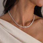 A woman showcases the elegance of personalized jewelry by wearing the Diamond Tennis Initial Necklace with an asymmetric clasp, styled over an off-shoulder cream top.