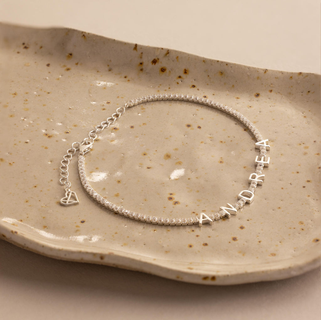 Diamond Tennis Letter Bracelet featuring the name ANDREA in sparkling letter charms, elegantly displayed on a speckled ceramic dish.