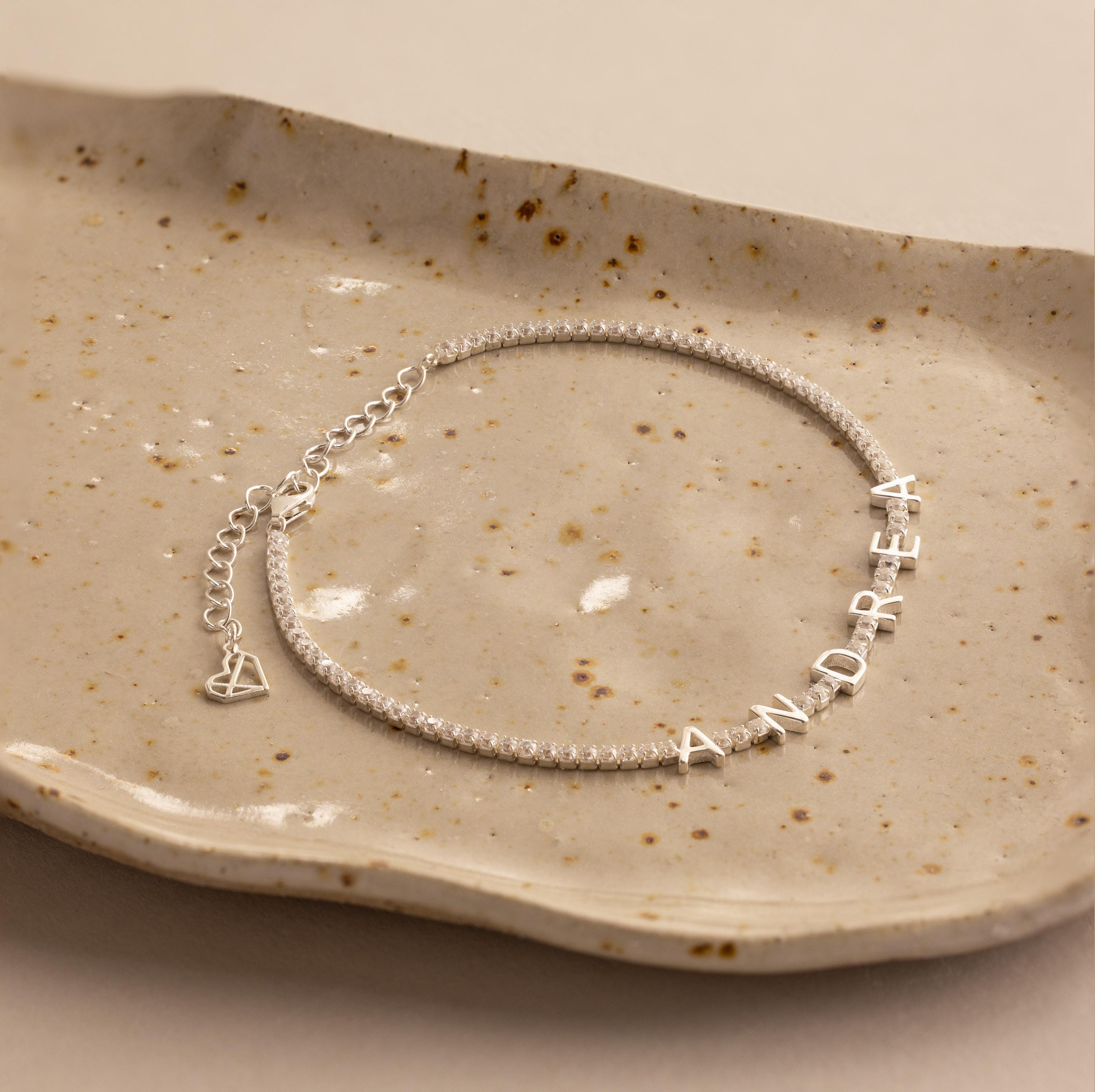 Diamond Tennis Letter Bracelet featuring the name ANDREA in sparkling letter charms, elegantly displayed on a speckled ceramic dish.