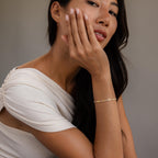 A woman in a white top rests her hand on her face, showcasing the Diamond Tennis Letter Bracelet as she looks at the camera.