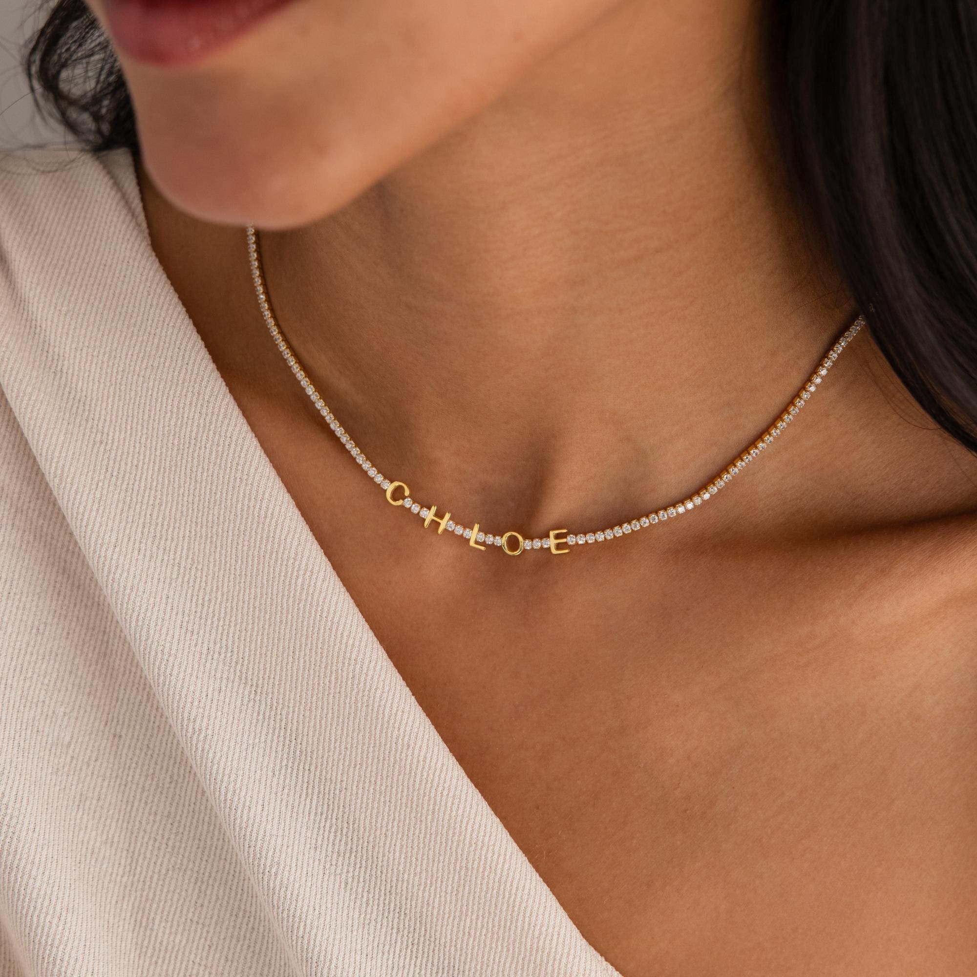 Close-up of a woman's neck wearing the Diamond Tennis Letter Necklace, personalized with "hope" in sparkling diamonds—an elegant custom piece that highlights both style and individuality.