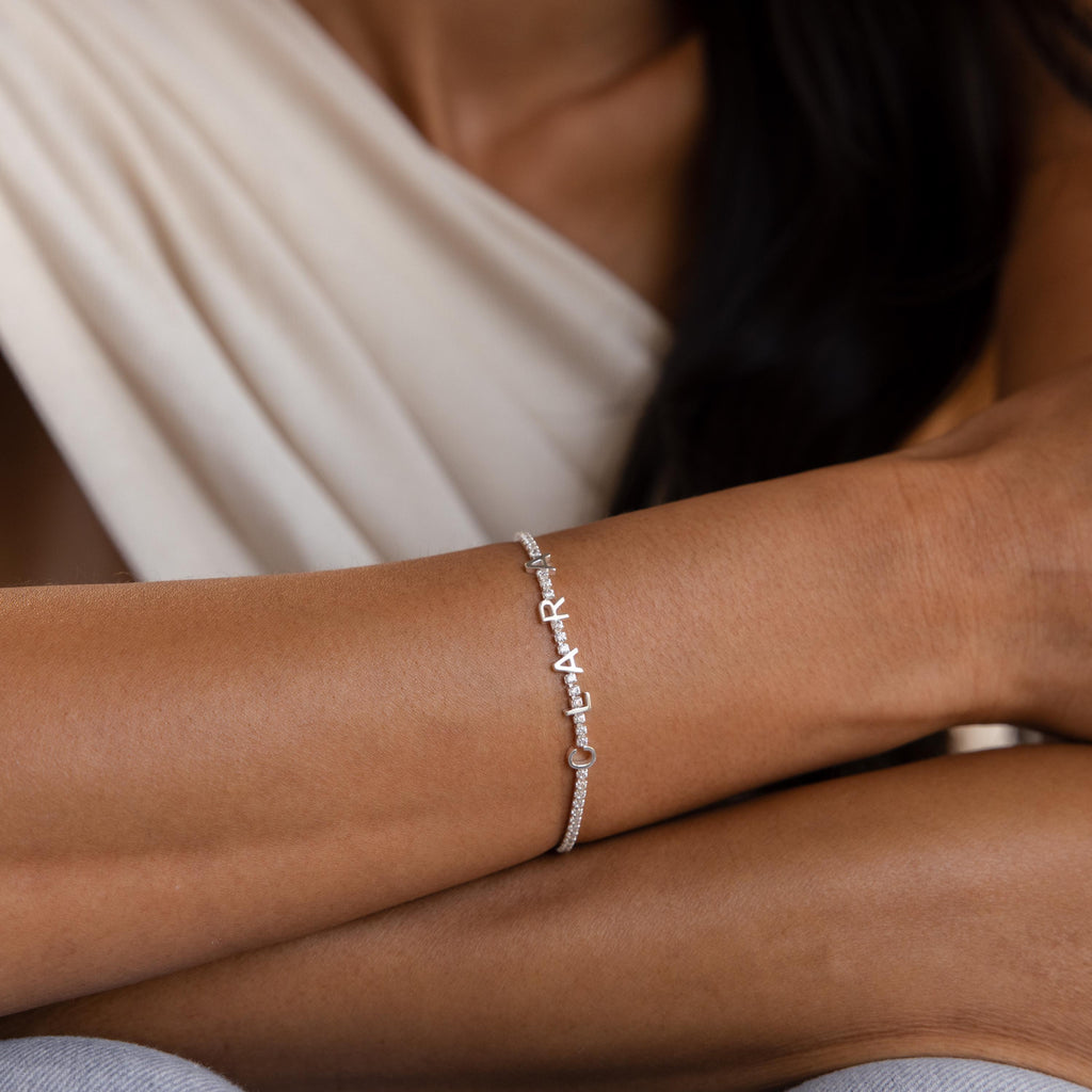 A close-up of a woman's arm wearing the Diamond Tennis Letter Bracelet, featuring small sparkling accents—perfect for those who love a minimalist bracelet style.