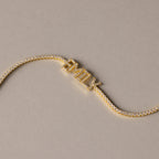 The Pave Name Tennis Bracelet showcases "EMILY" in sparkling diamond-studded letters, creating a stunning personalized bracelet set against a beige background.