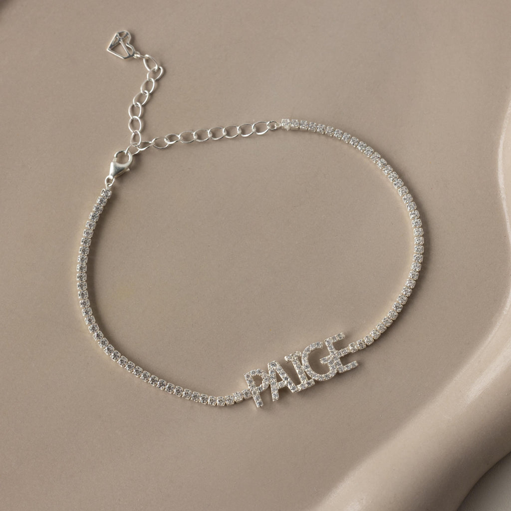 The Pave Name Tennis Bracelet features sparkling stones and the name PAIGE in capital letters—a stunning personalized accessory for any occasion.