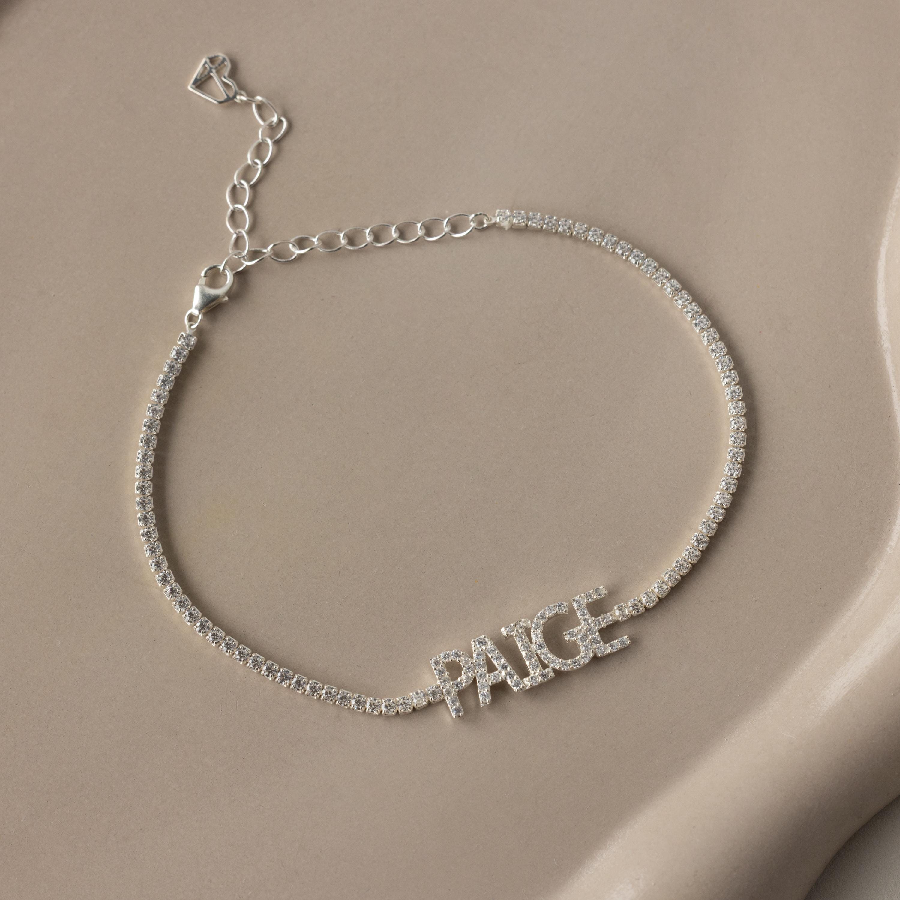 The Pave Name Tennis Bracelet features sparkling stones and the name PAIGE in capital letters—a stunning personalized accessory for any occasion.