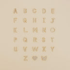 Gold and pearl alphabet letters, a heart, and a butterfly arranged on beige—perfect inspiration for designing your own Diamond Tennis Initial Bracelet or stacking it with others.