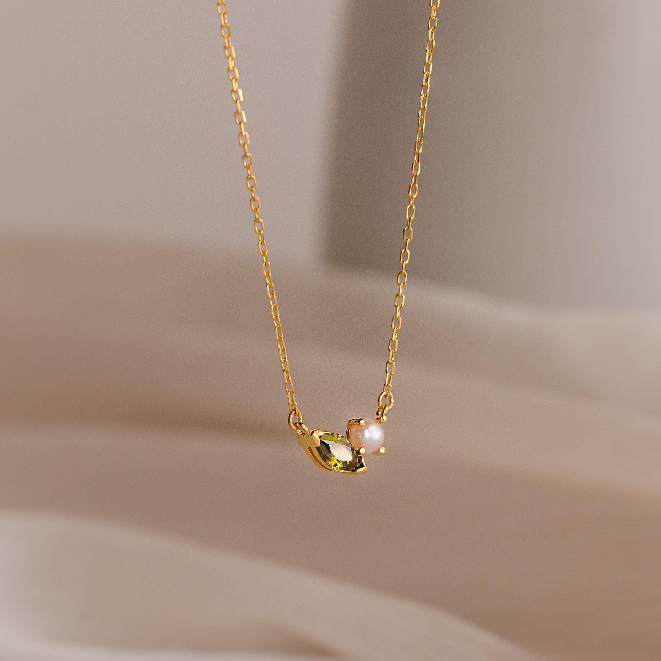 The Marquise Birthstone & Pearl Necklace features a gold chain, a leaf-shaped charm, and a small pearl—an elegant customizable birthstone necklace ideal for personalizing your look.