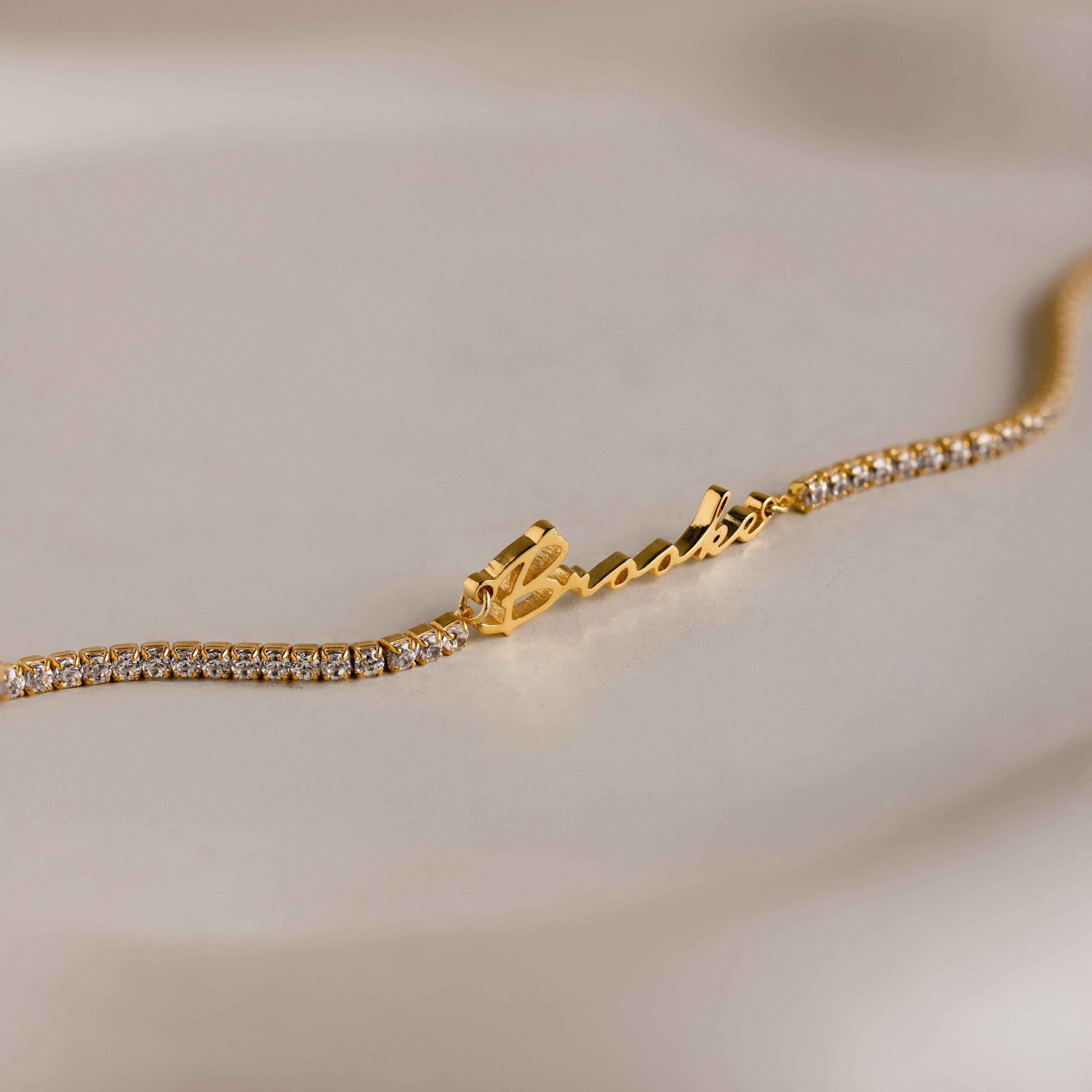 The Venice Name Tennis Bracelet features a cursive nameplate and a band of small sparkling diamonds, displayed on a neutral background.