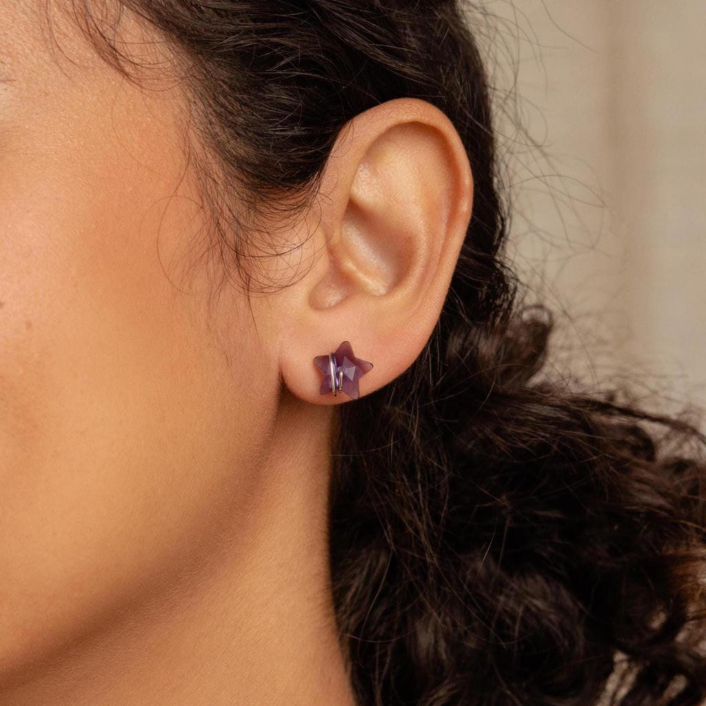 Close-up of model wearing a purple star-shaped earring in silver. 