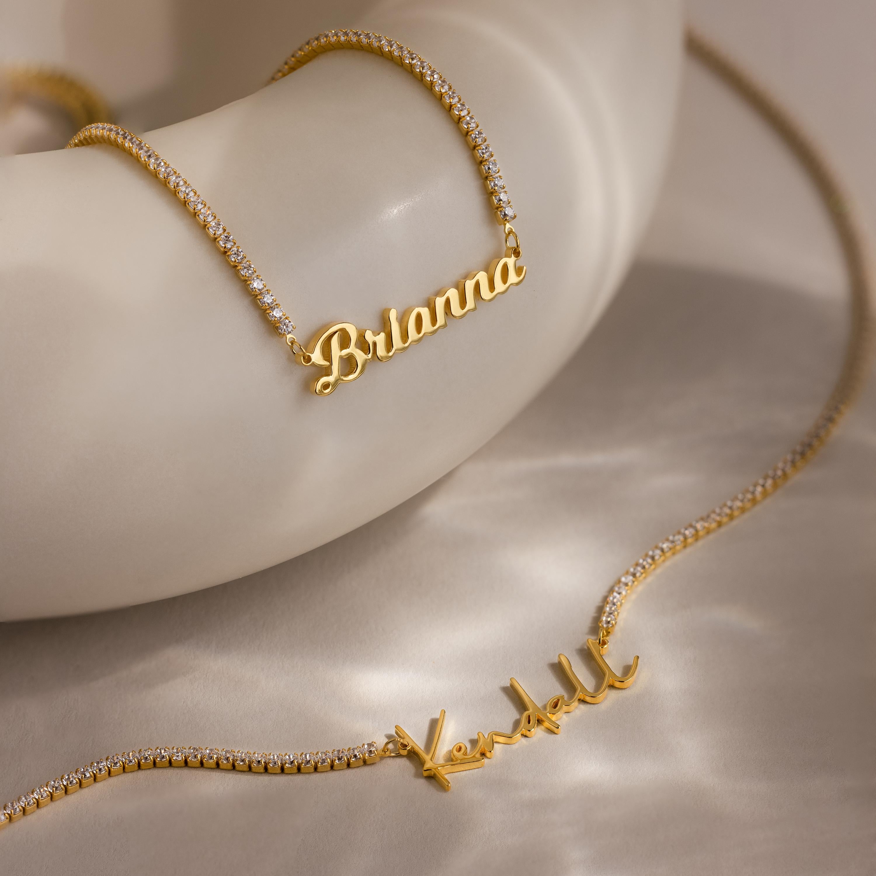 Two Diamond Tennis Name Necklaces, personalized with "Brianna" and "Kendall," are shown on a smooth surface—elegant custom pieces reflecting the latest nameplate jewelry trend.