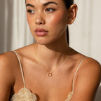 Woman wearing the Pave Amethyst Charm Clip, a gold necklace with a circular pendant, looking to the side in soft natural light—an elegant example of customizable jewelry.