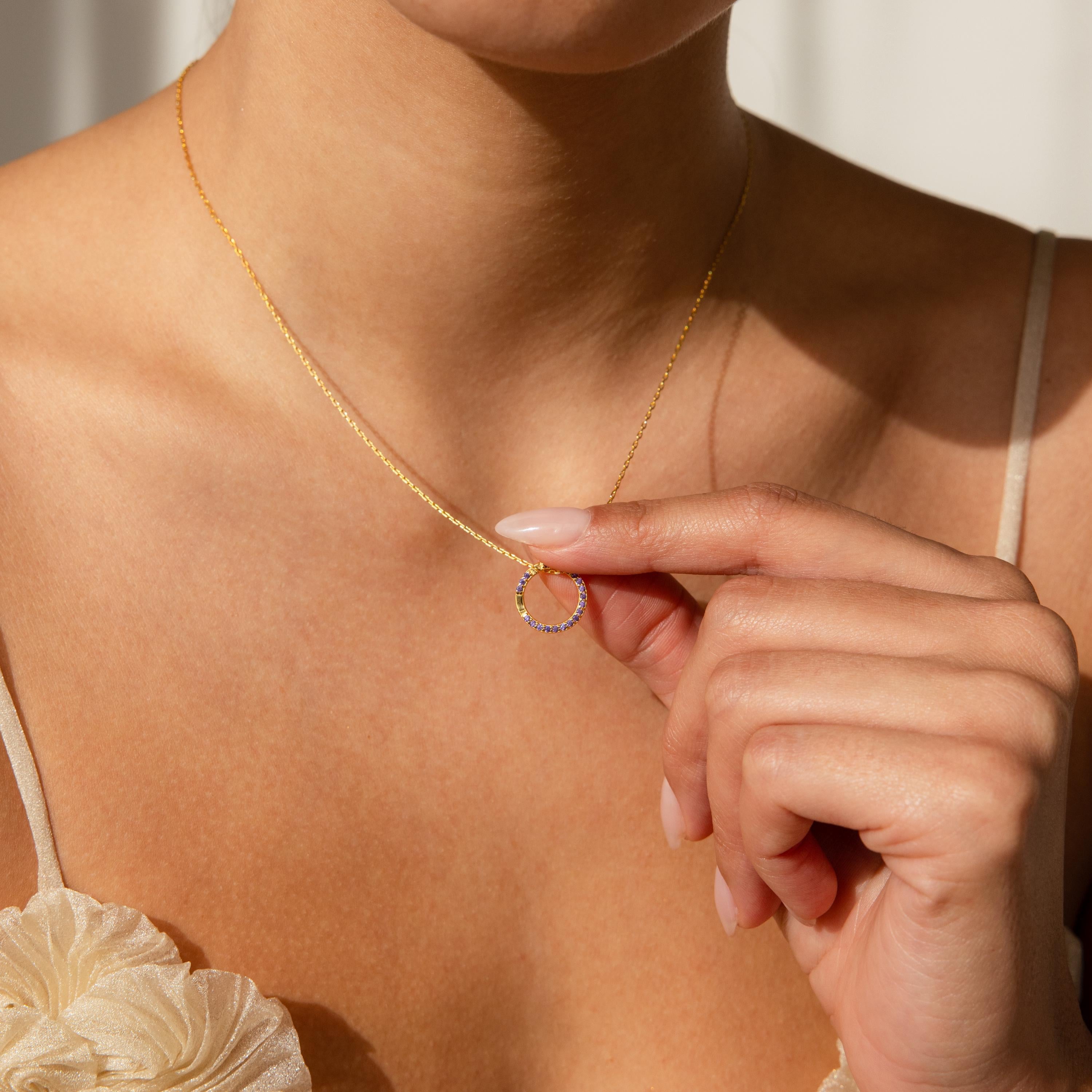 A woman delicately holds a gold necklace with a small circular pendant—an ideal pairing for personalized jewelry like the Pave Amethyst Charm Clip.
