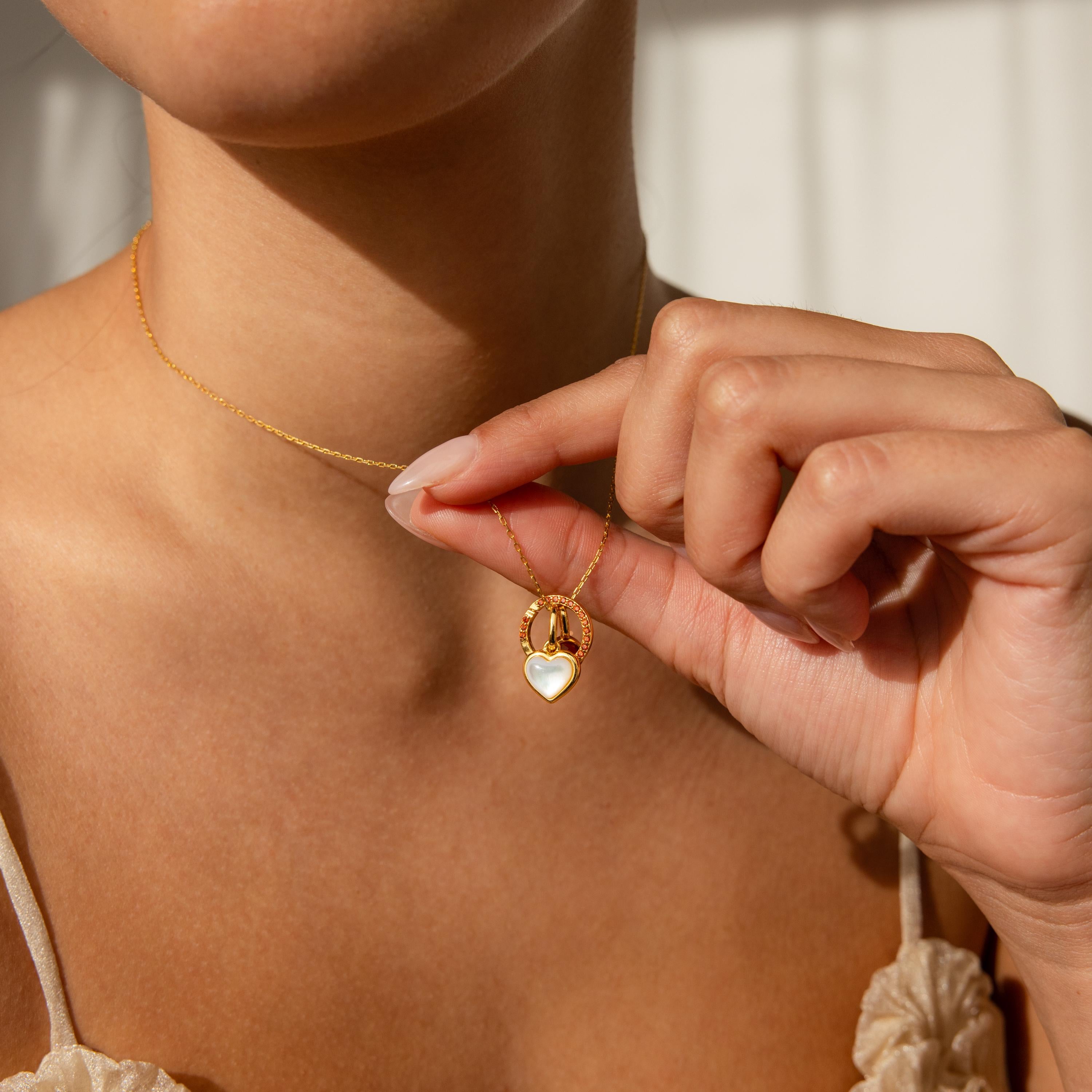 A woman holds a Pave Garnet Charm Clip on a delicate necklace close to her neck, showcasing her unique jewelry personalization.