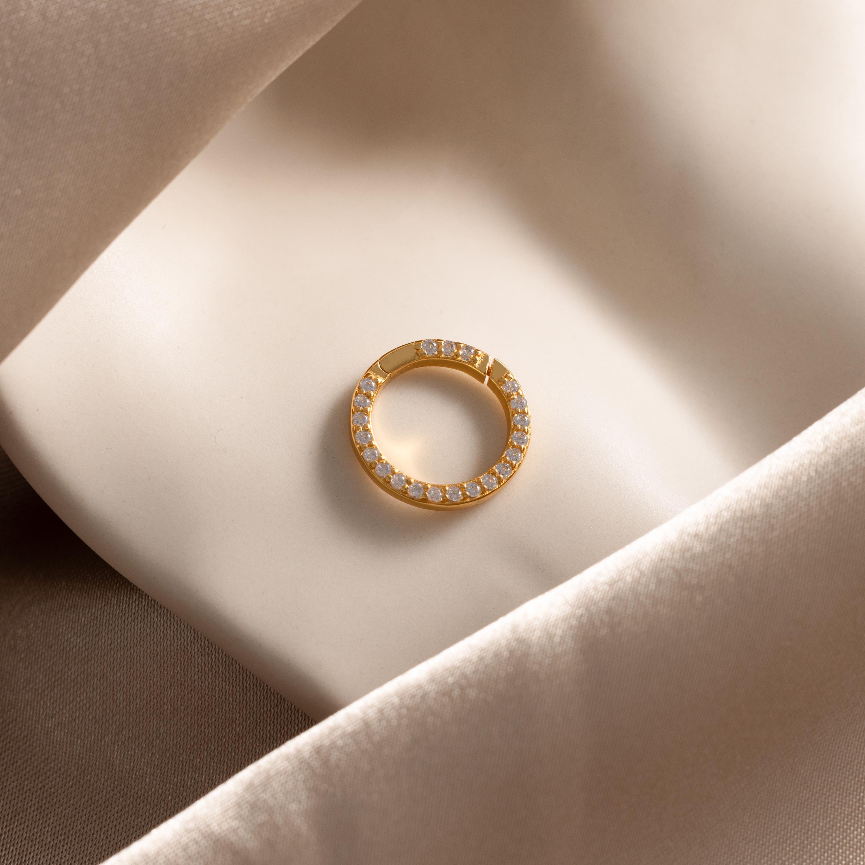 The Pave Diamond Charm Clip, featuring sparkling diamonds, rests on smooth cream-colored satin—ideal for pairing with a personalized jewelry charm holder or a delicate birthstone ring charm.