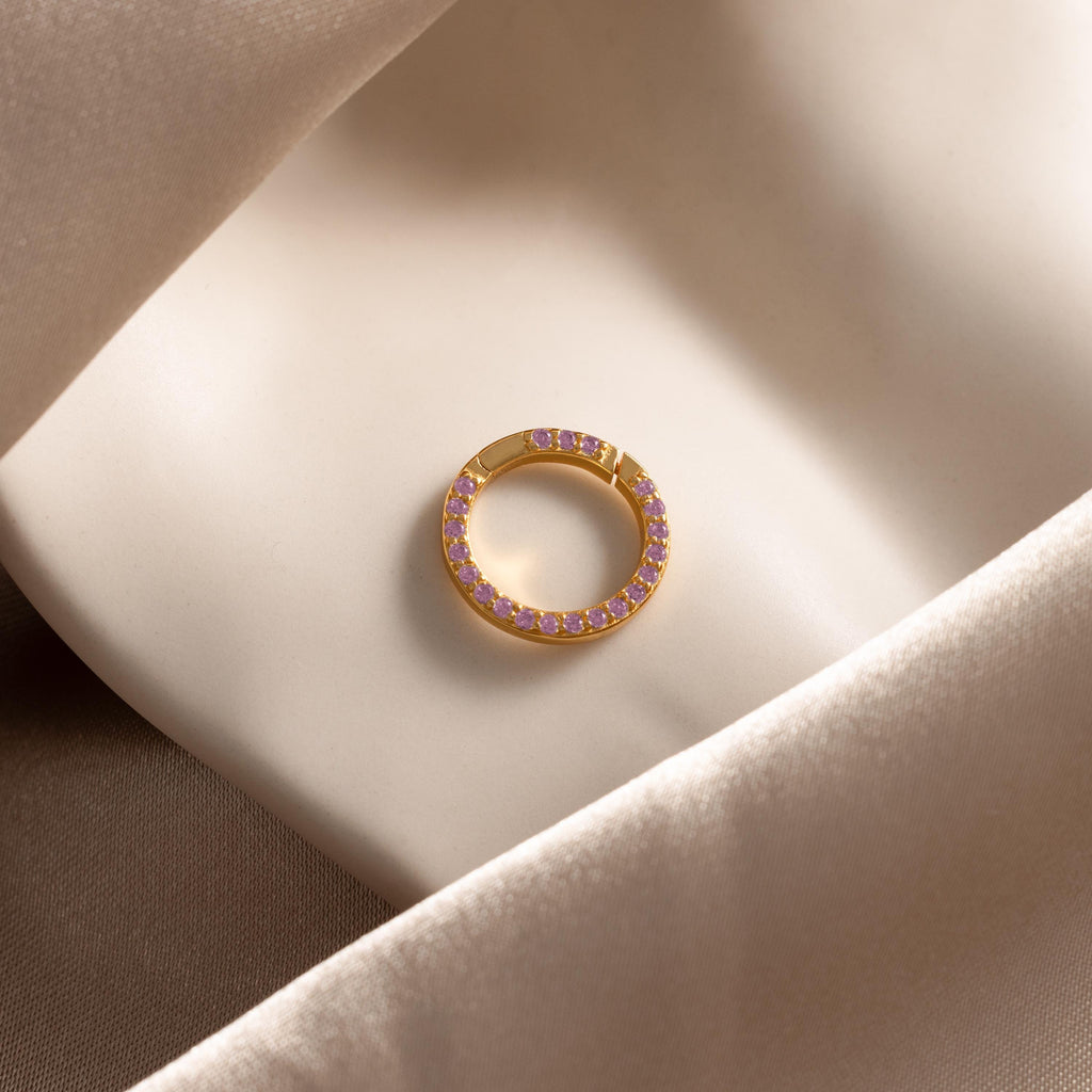 The Pave Pink Tourmaline Charm Clip, sparkling with pink stones, rests elegantly on soft beige satin fabric.
