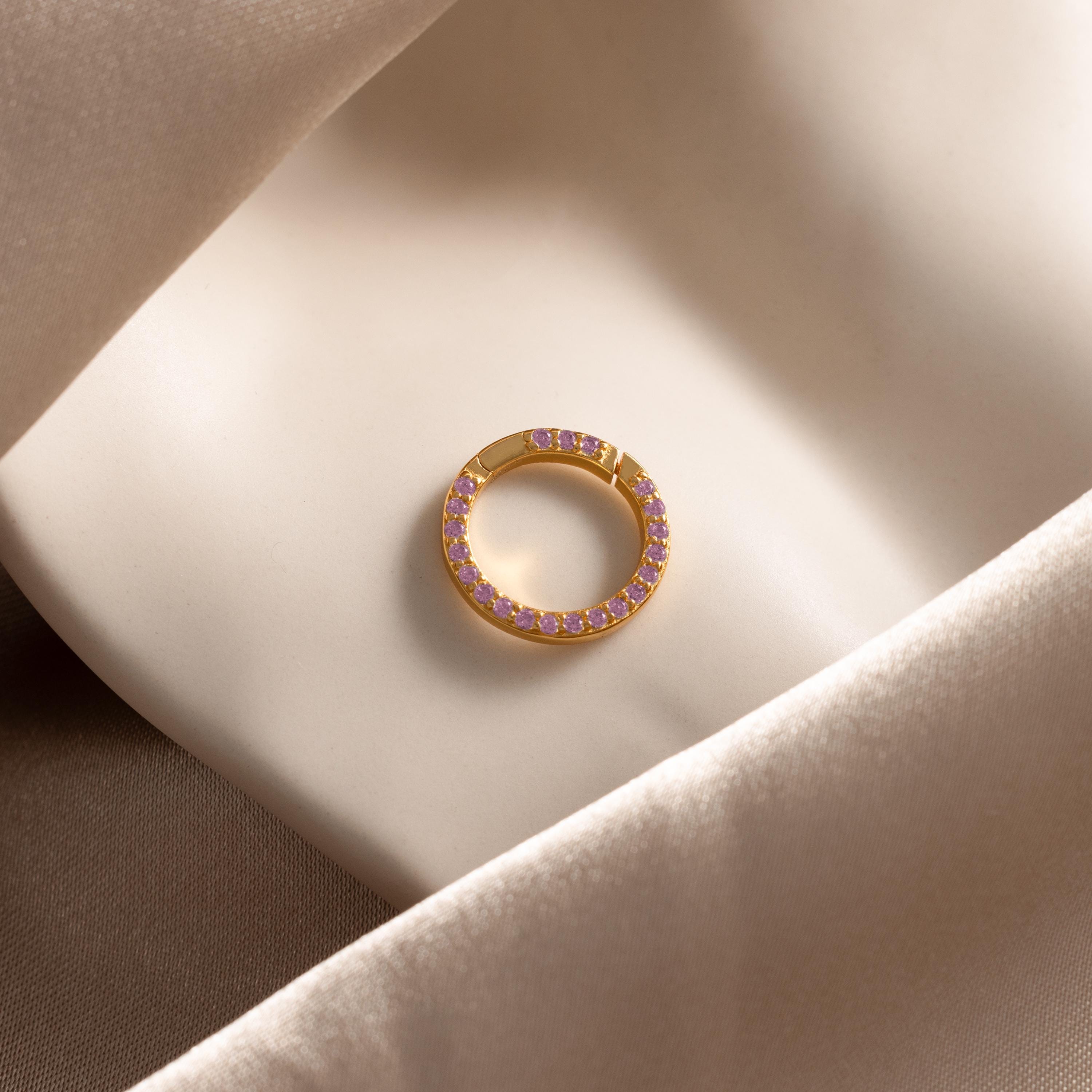 The Pave Pink Tourmaline Charm Clip, sparkling with pink stones, rests elegantly on soft beige satin fabric.