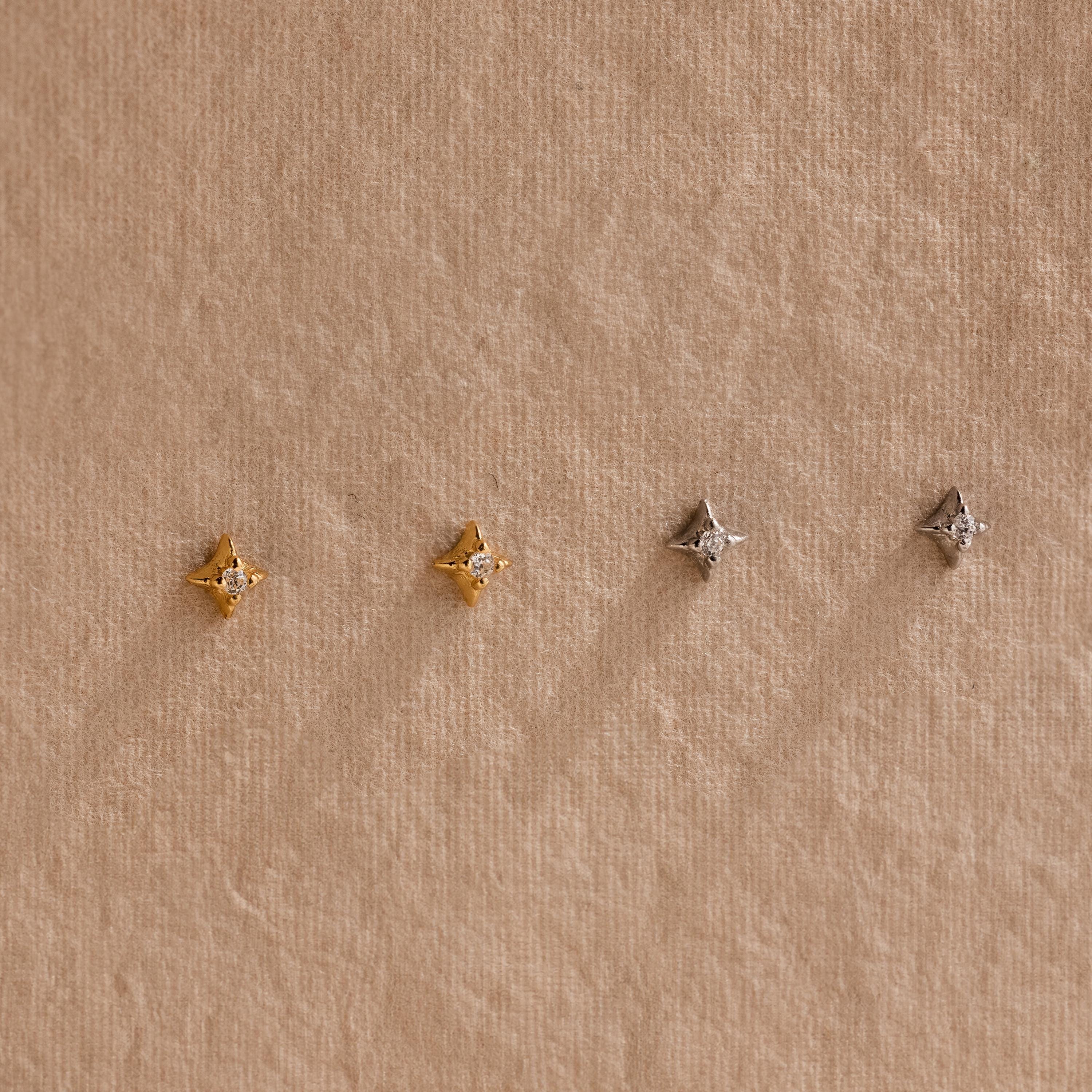 Two pairs of of gold and silver North Star Stud earrings hanging