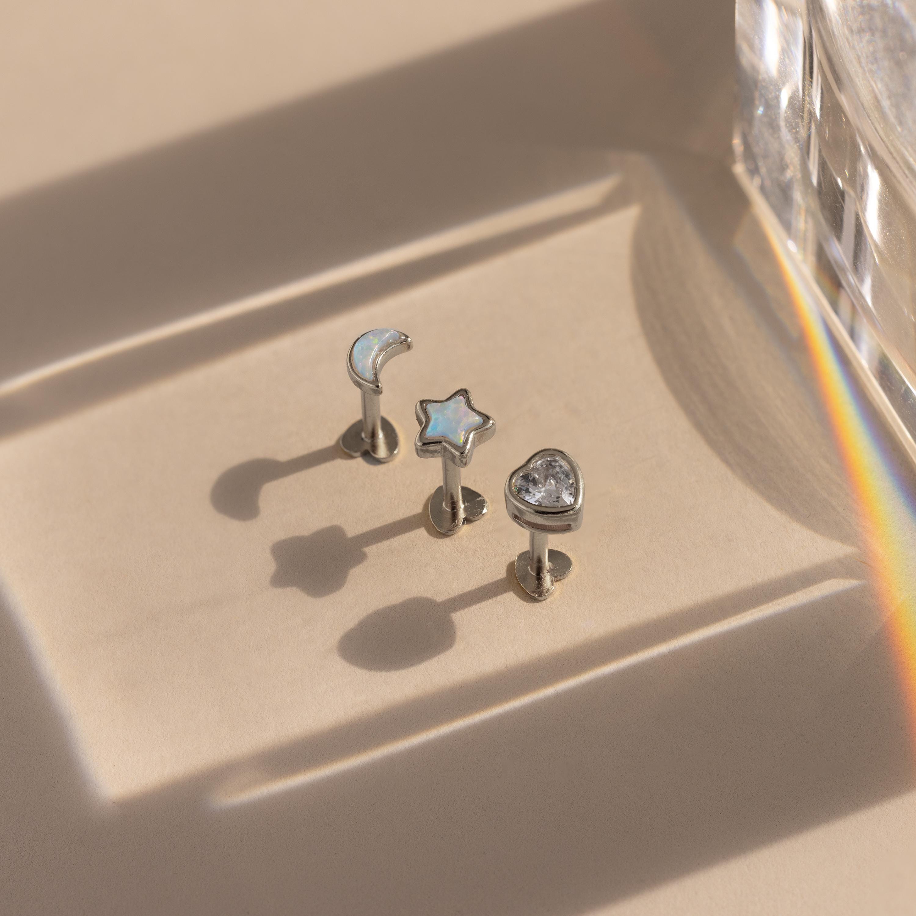 Flat lay of 3 mismatched silver moon, star, and heart stud earrings with opal and CZ diamond