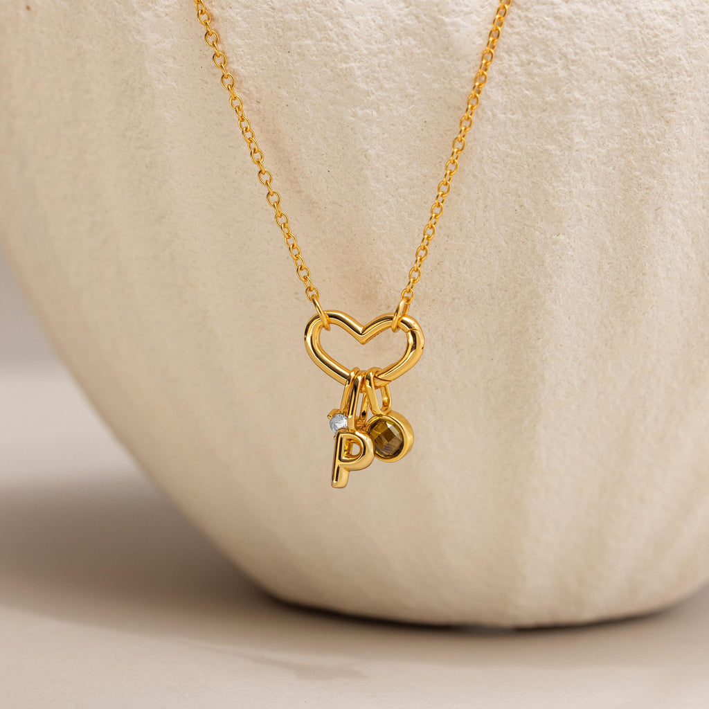 The Heart Carabiner Set in 18K Gold features a heart-shaped pendant, heart carabiner, and small P and circular charms—an elegant necklace to enhance any jewelry collection.