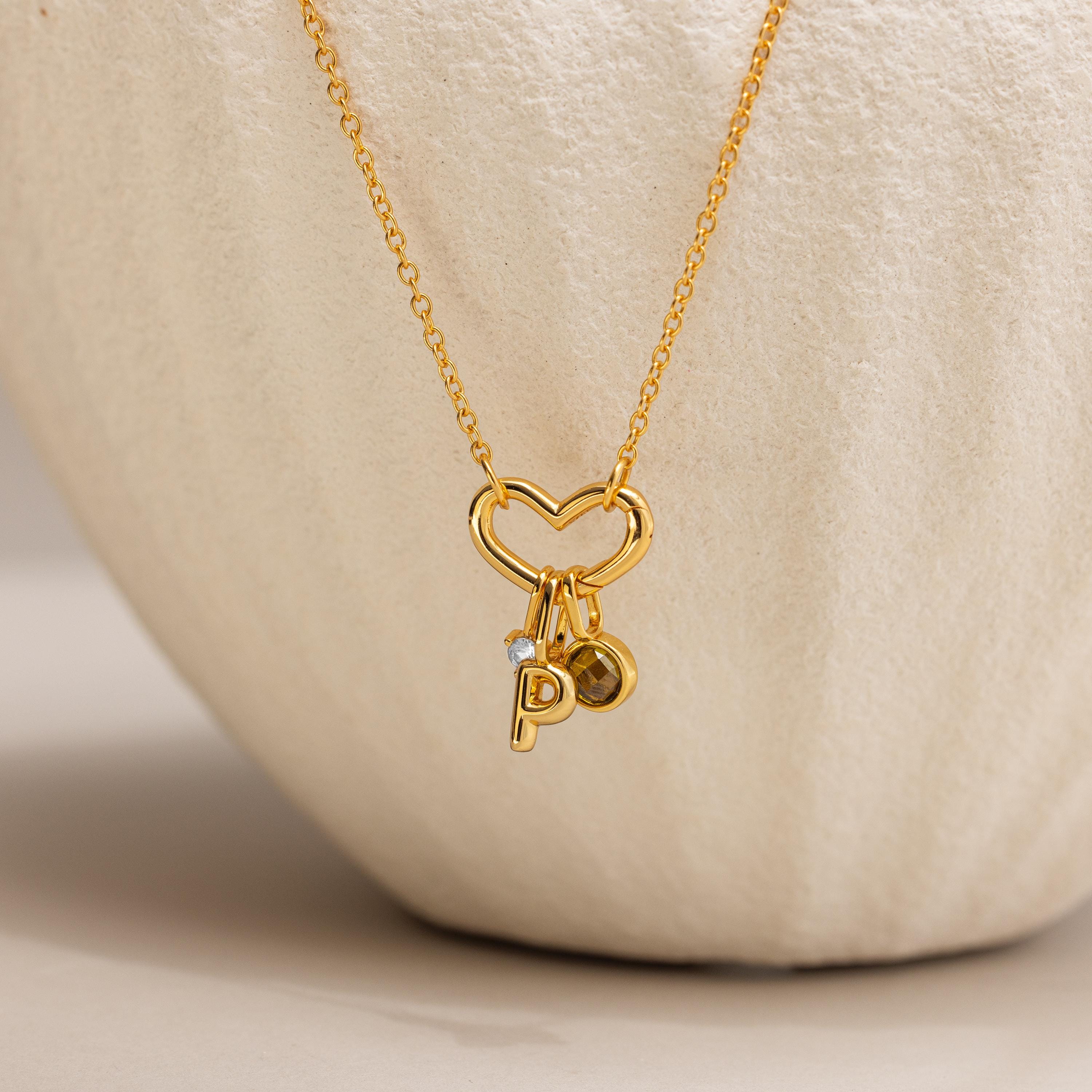 The Heart Carabiner Set in 18K Gold features a heart-shaped pendant, heart carabiner, and small P and circular charms—an elegant necklace to enhance any jewelry collection.