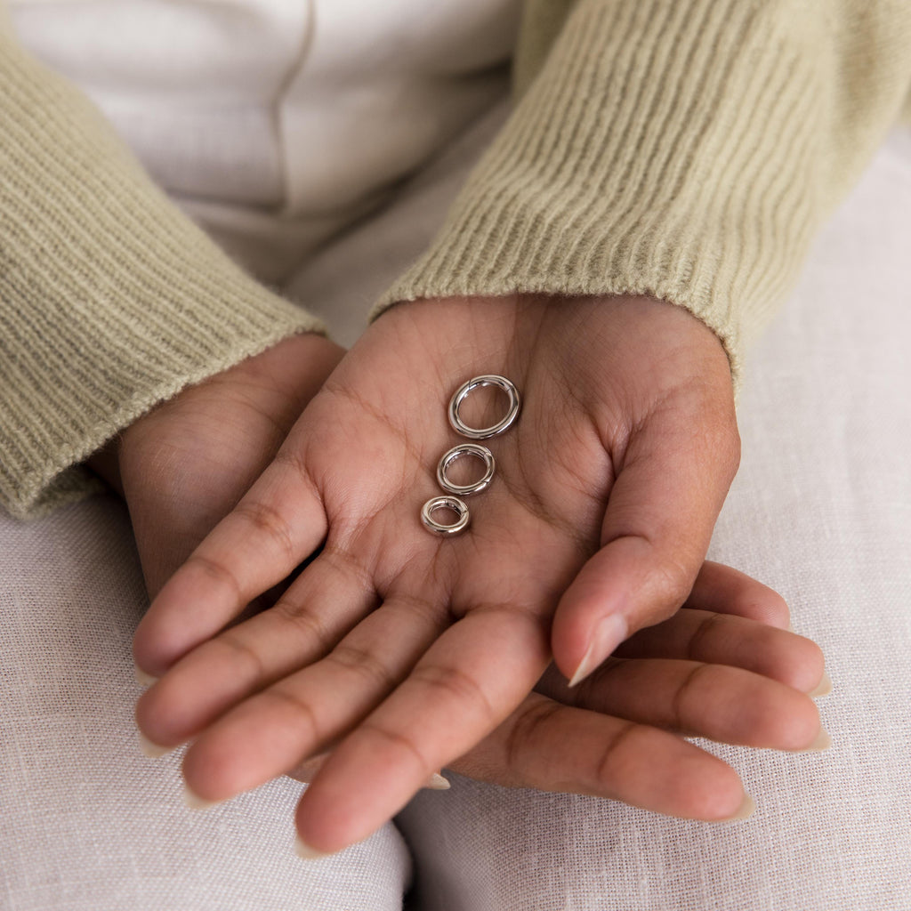 A person holds the Round Carabiner Charm Set in Sterling Silver—three rings of different sizes—in their open palm, while wearing a beige sweater.