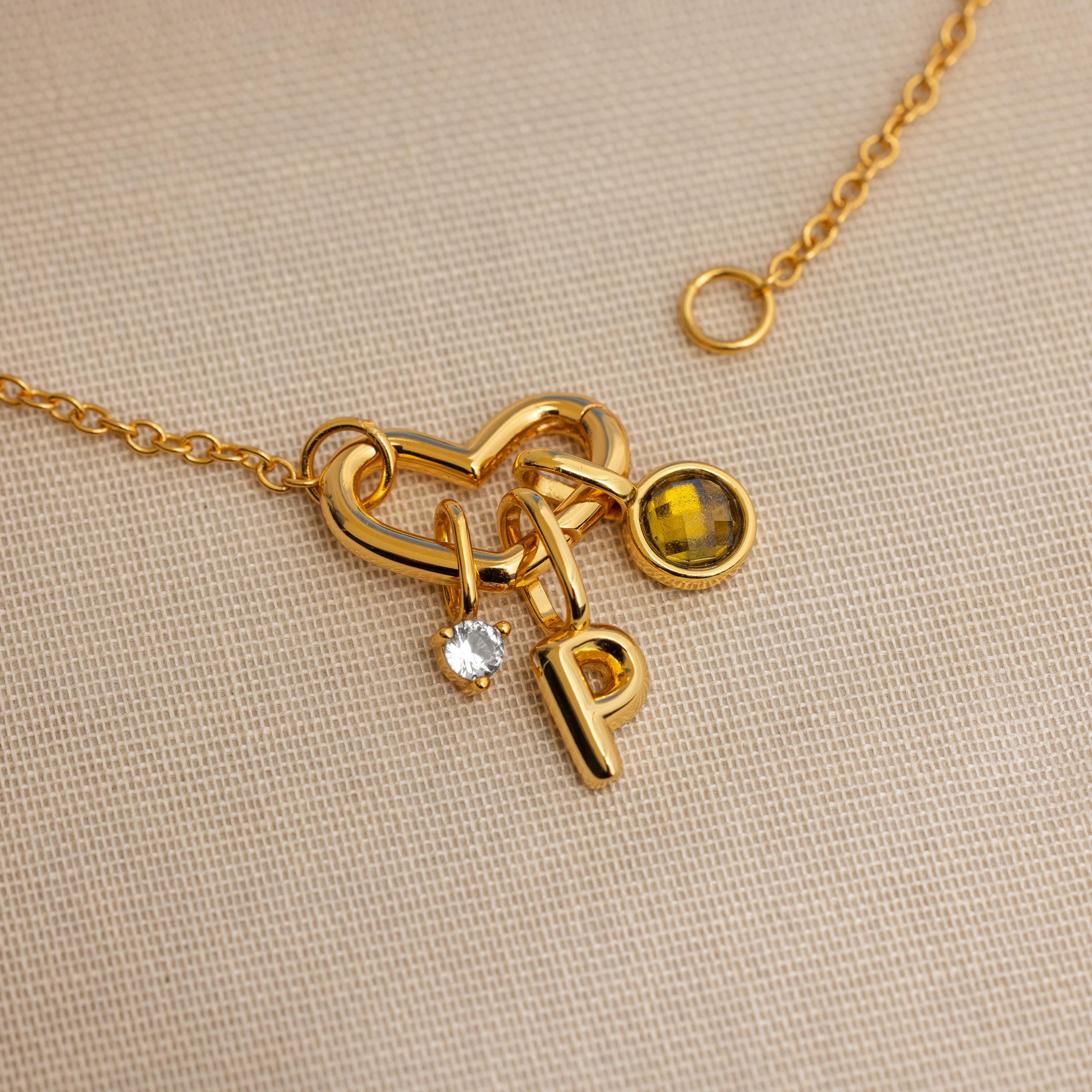 The Heart Carabiner Set in 18K Gold features a heart-shaped clasp, letter P, clear gem, and yellow gemstone charm—ideal for mixing with your jewelry or as a unique charm bracelet connector.