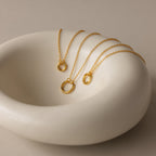 The Round Carabiner Charm Set in 18K Gold, featuring circular pendants, is displayed on a smooth, white ceramic dish.