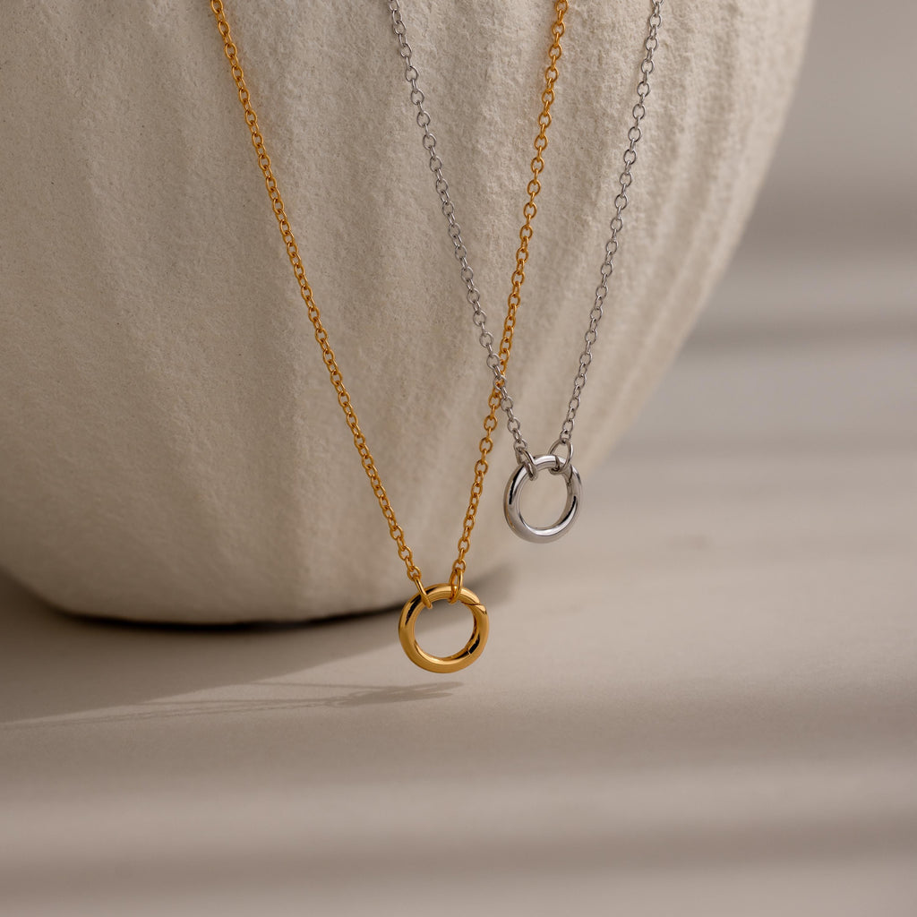 Cable Circle Charm Necklaces in gold and silver are shown on a textured white background, each necklace offering a subtle yet stylish statement.