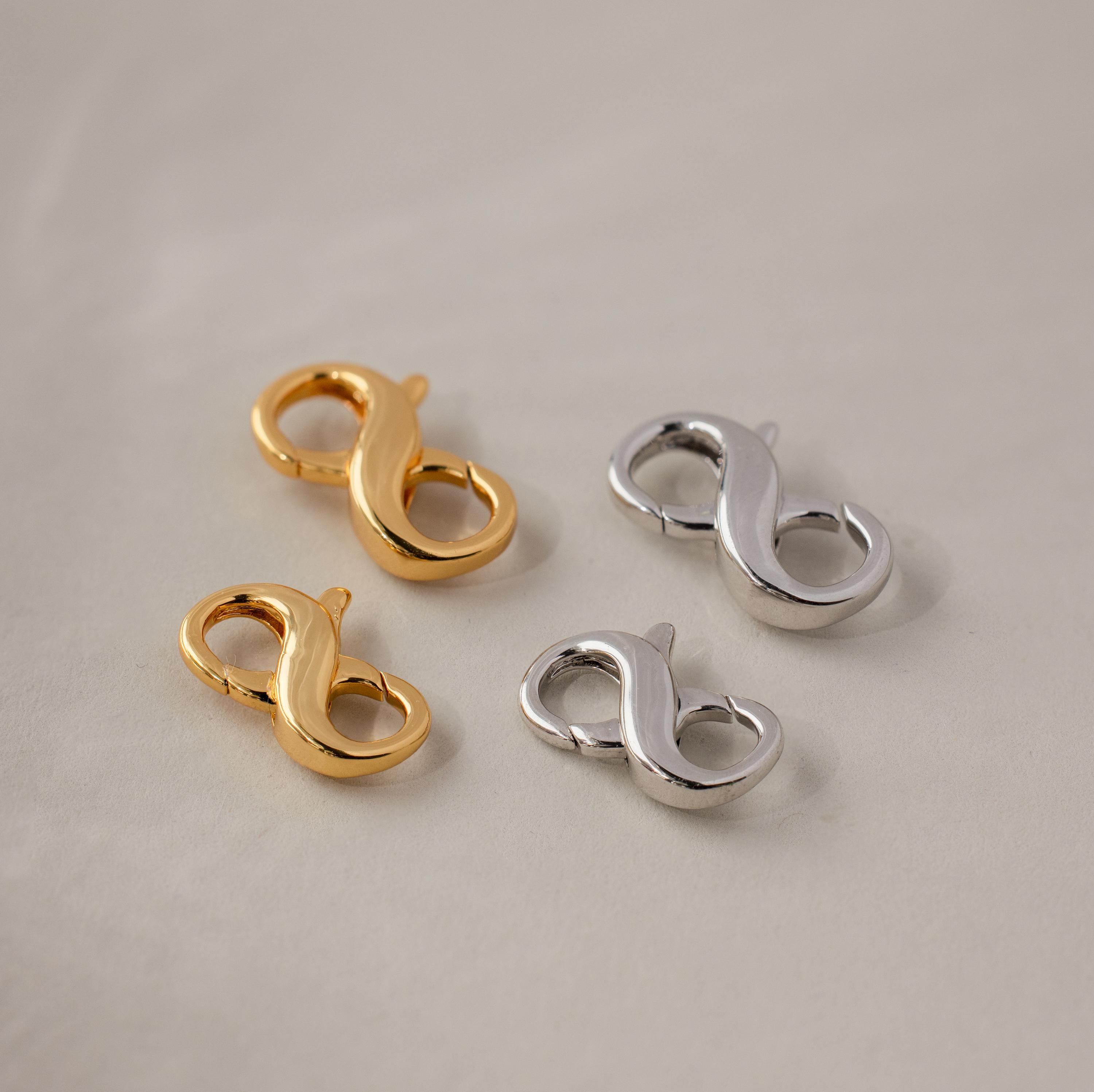 The Multipurpose Lobster Clasp Extender Set in White Gold includes two gold and two silver infinity-shaped extenders, displayed on a light textured surface—ideal as charm holders for your favorite jewelry pieces.
