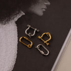 The Bar & Carabiner Charm Set in White Gold features four metal jewelry pieces in silver and gold, displayed on a magazine page with a black-and-white portrait.